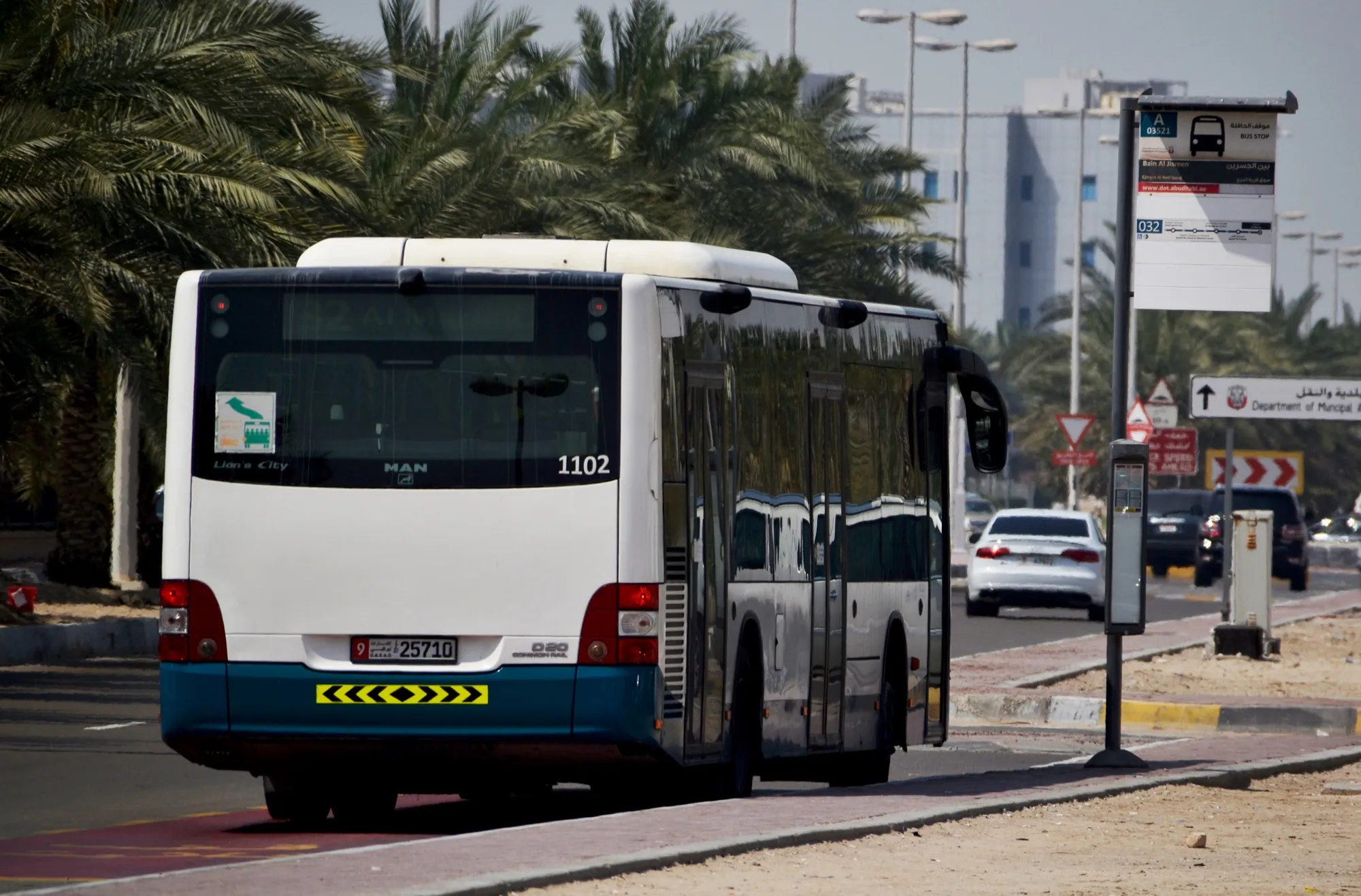 A city bus at a bus stop on a palm-lined street in Abu Dhabi