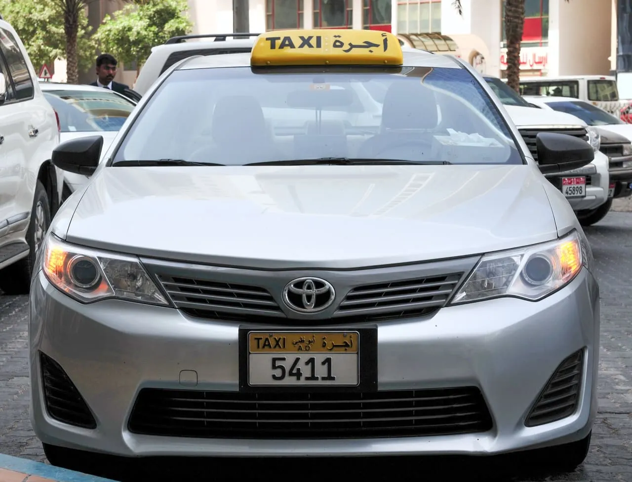A silver Toyota taxi with an Abu Dhabi taxi number plate and a yellow roof sign