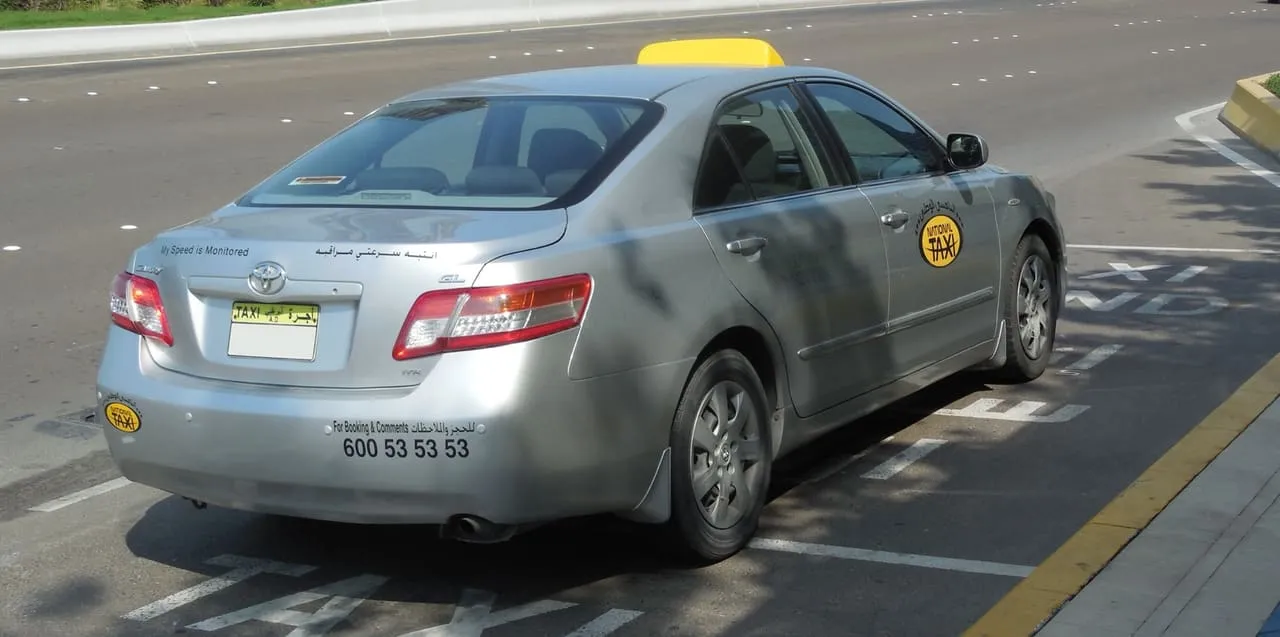 A silver Abu Dhabi taxi with a yellow roof sign