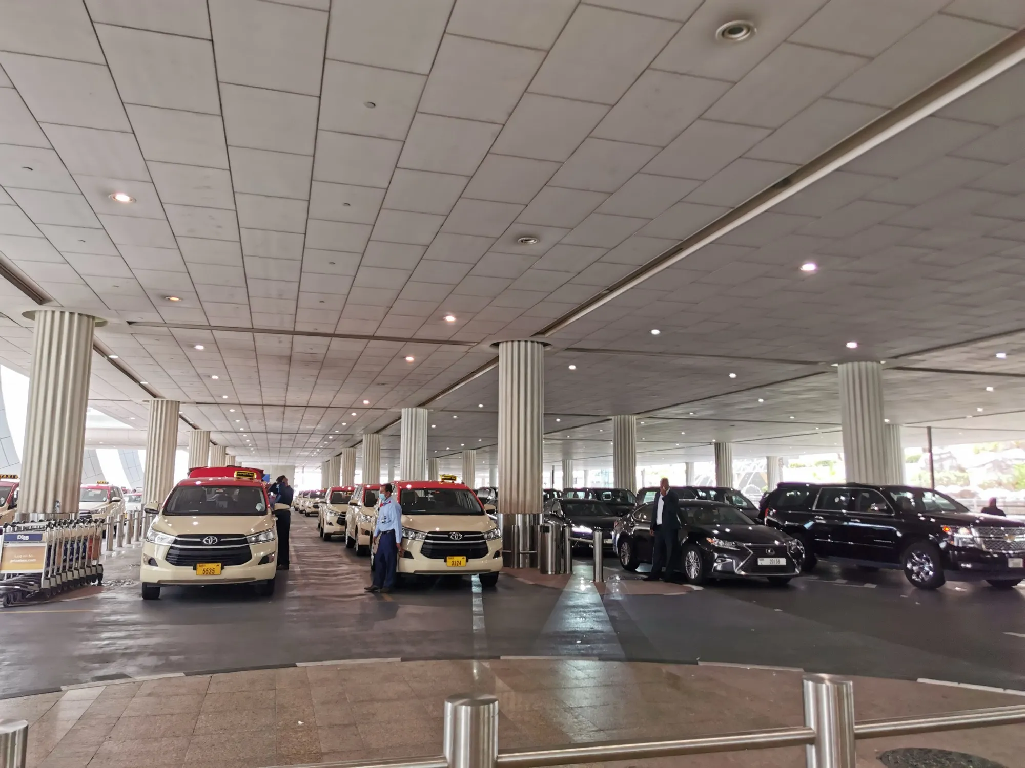 Dubai taxis and black chauffeur cars lined up under the covered pick-up area at Dubai International Airport