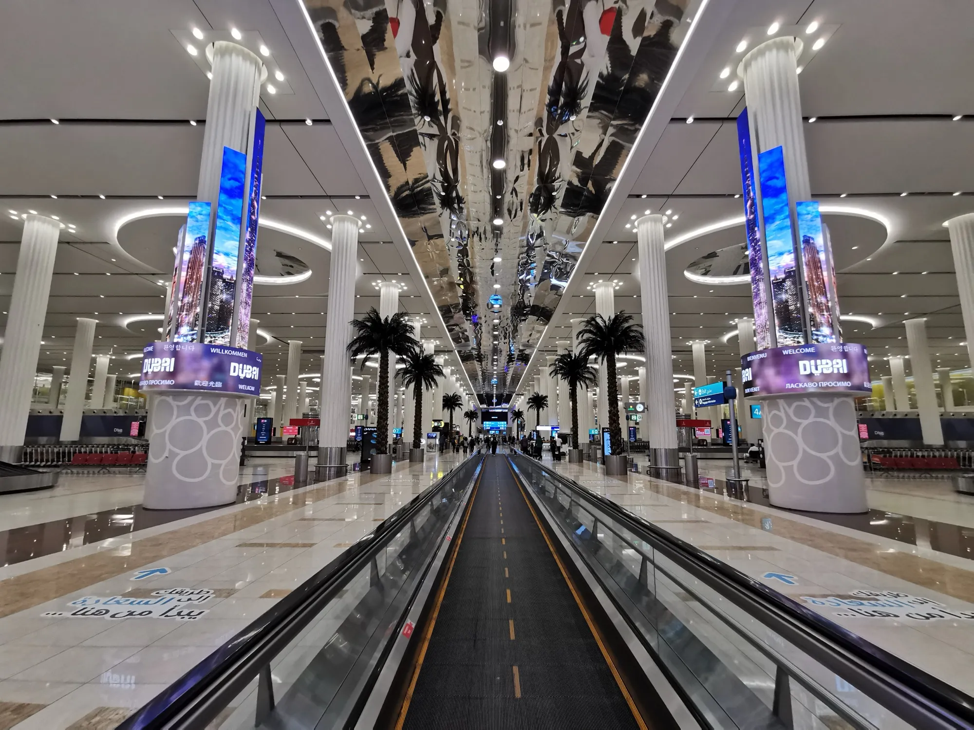 Travelator through the baggage reclaim hall at Dubai International, between screens reading Welcome to Dubai