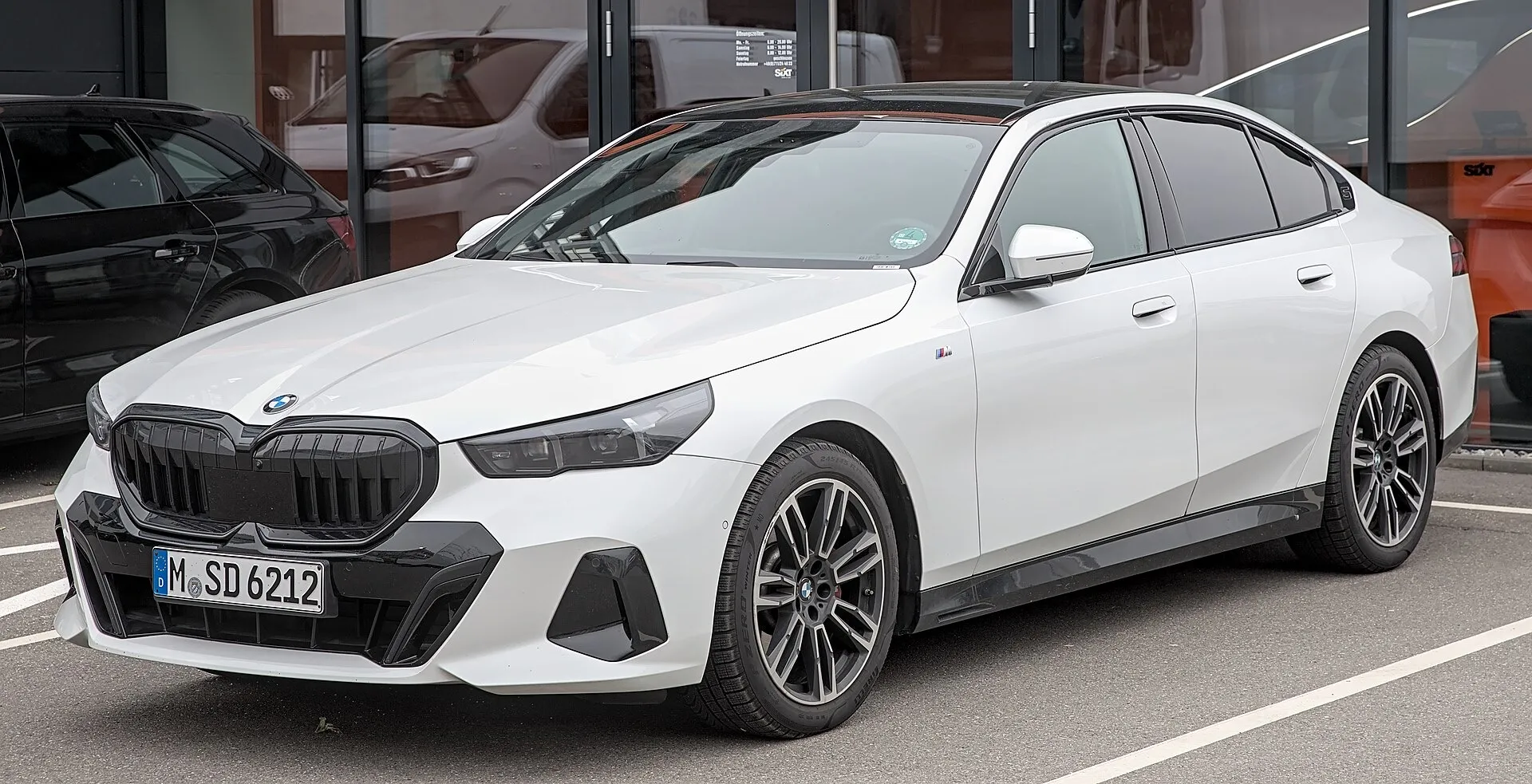 A white BMW 5 Series sedan parked in a car park, seen from the front left