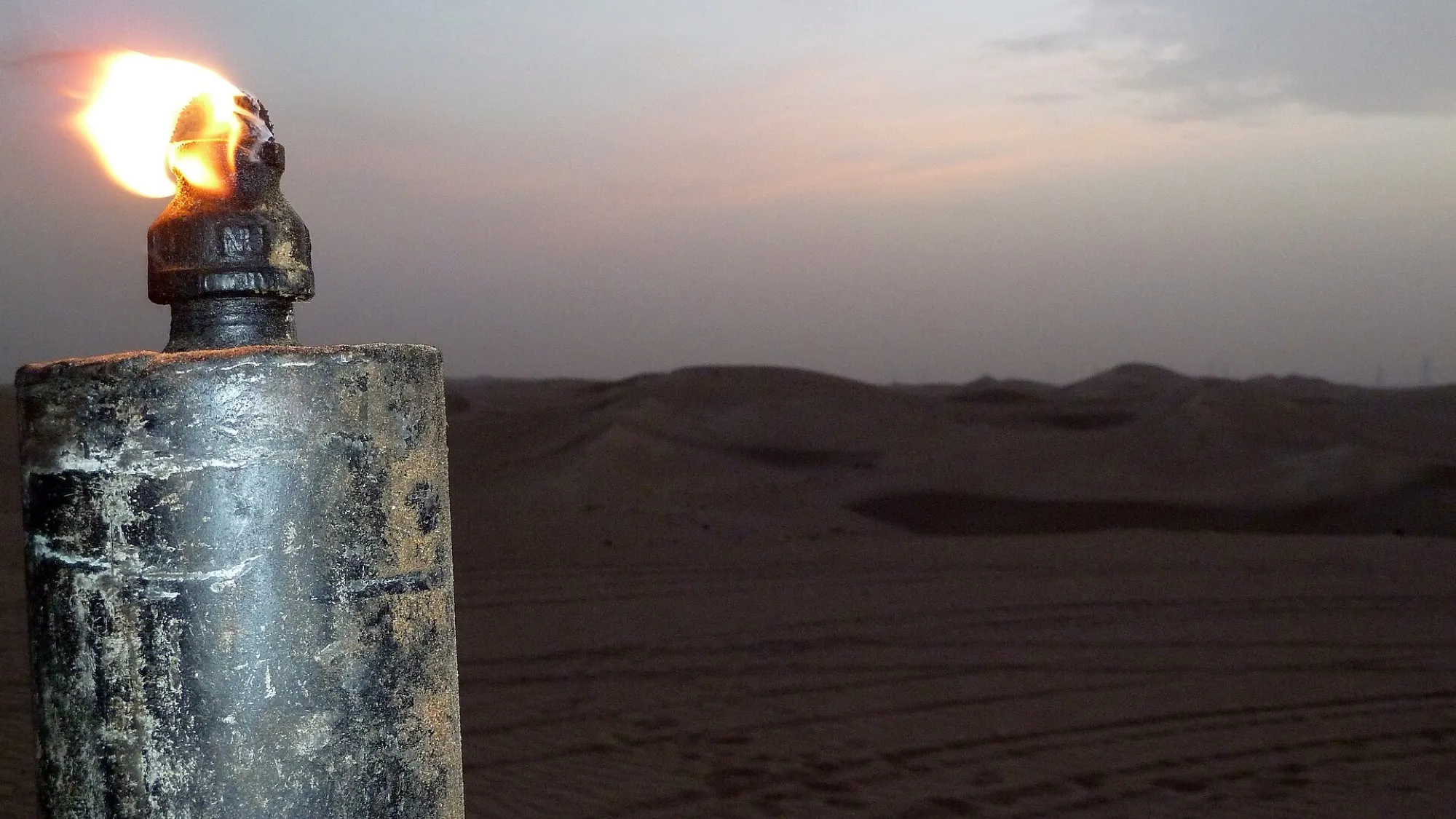 A lit torch on a post at dusk, looking out over the dunes of the Al Marmoum desert in Dubai