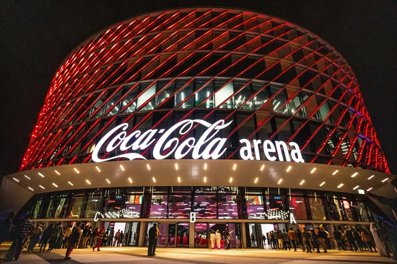 The Coca-Cola Arena in Dubai lit up at night, with people at the entrance
