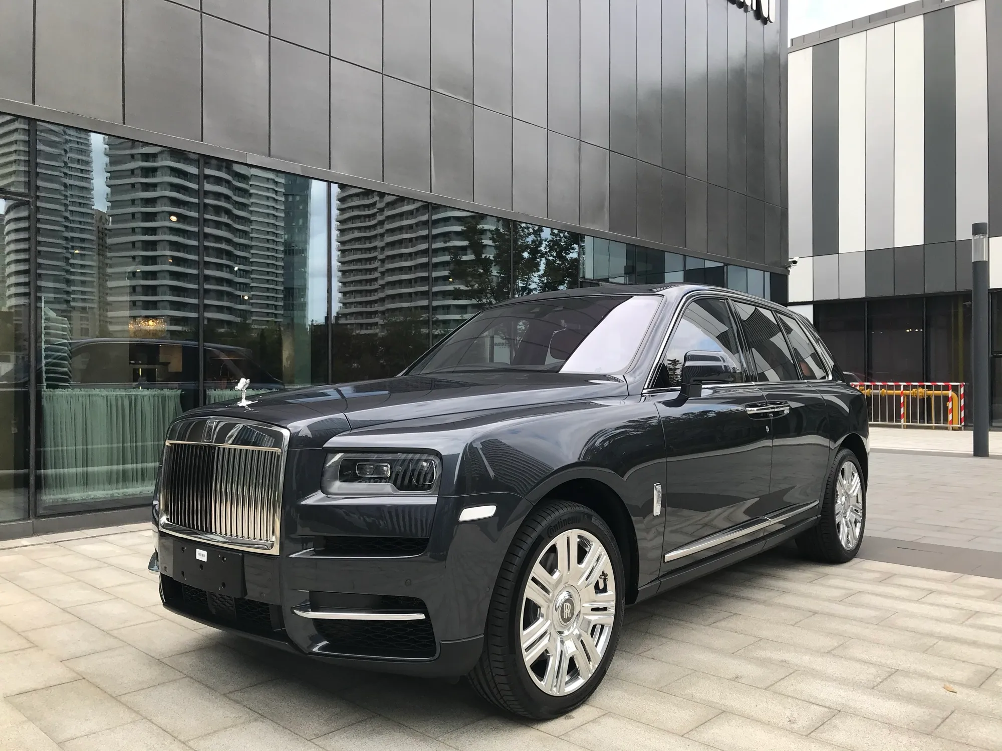 A grey Rolls-Royce Cullinan SUV parked in front of a glass-fronted building
