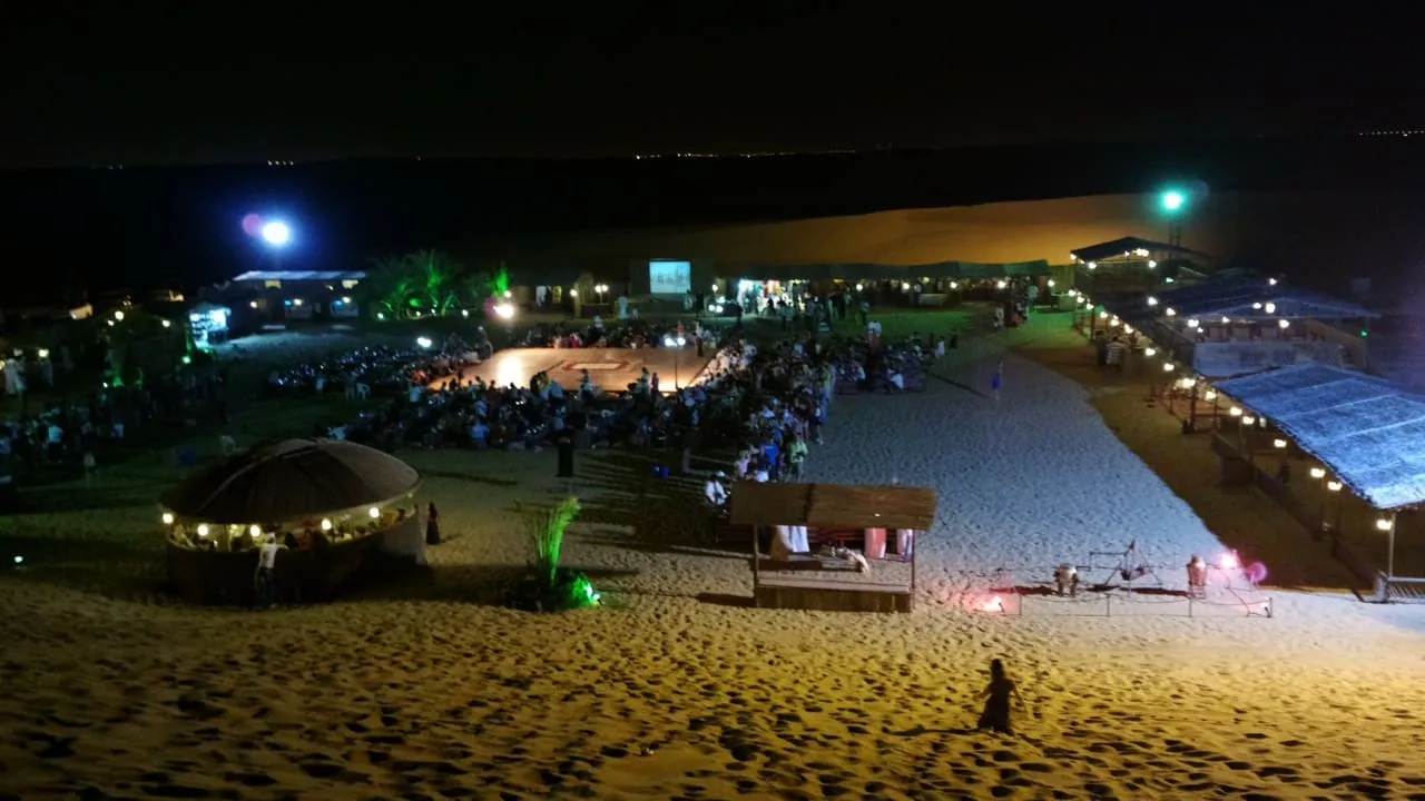 A desert camp at Al Awir, Dubai, lit up at night, with guests seated around the central stage
