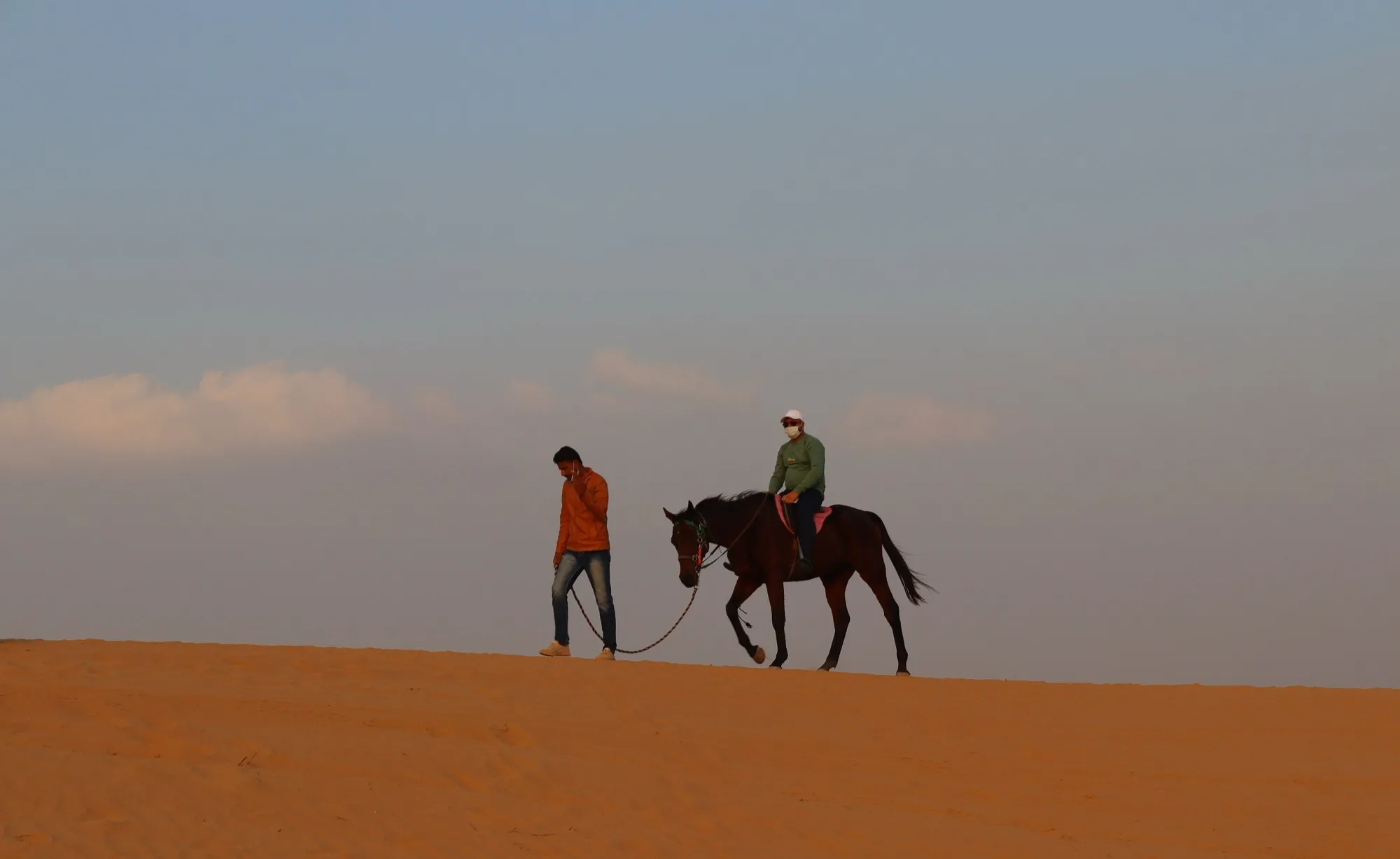 A guide leading a horse and rider across the dunes outside Dubai at dusk