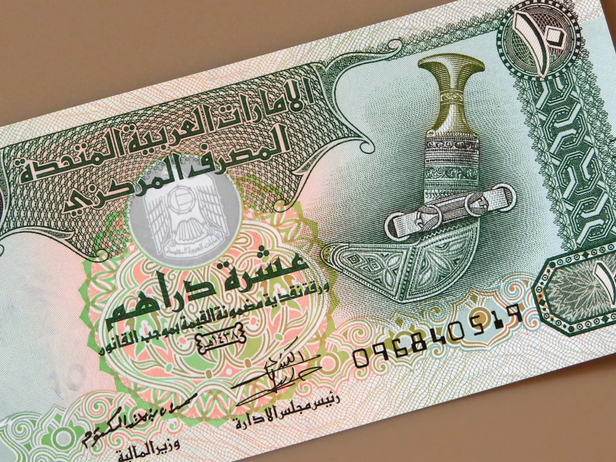 Close view of a UAE 10 dirham banknote showing Arabic text, the national emblem and a khanjar dagger