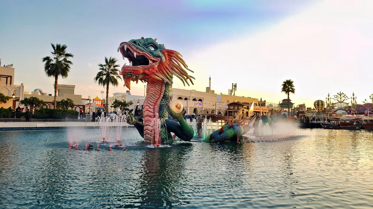 A giant dragon sculpture with fountains in the Global Village lake at sunset
