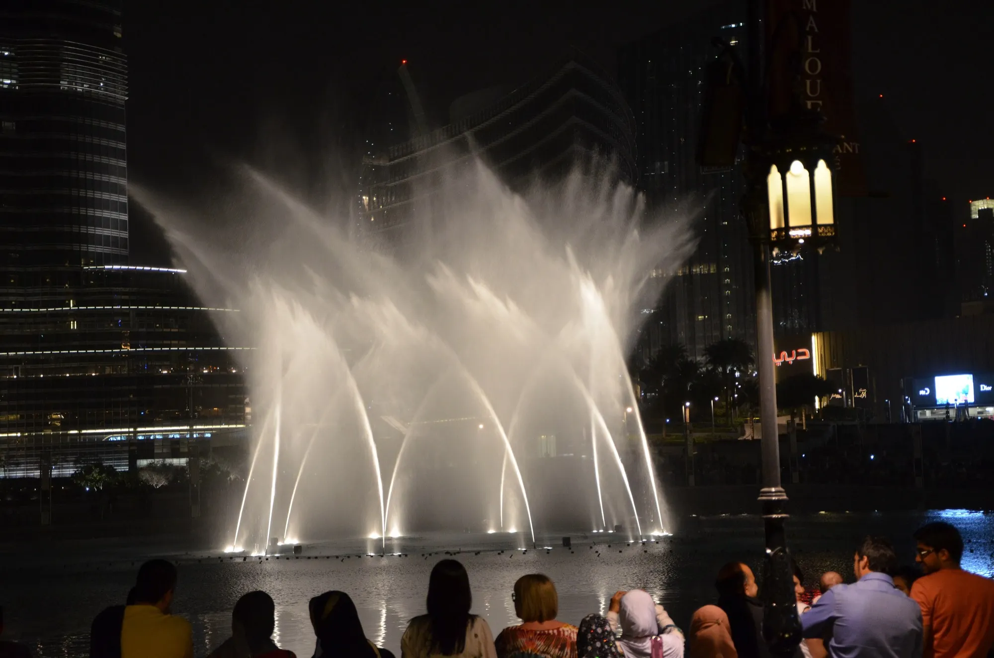 The Dubai Fountain lit up at night in Downtown Dubai while visitors watch from the waterfront