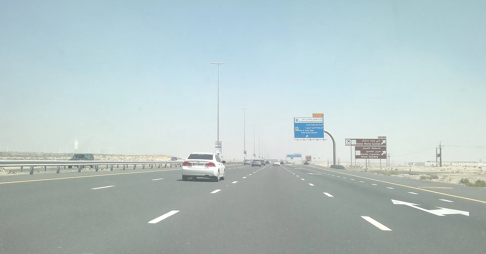 A multi-lane desert highway in Dubai with exit signs for Sheikh Mohammed bin Zayed Road and Dubai World Central