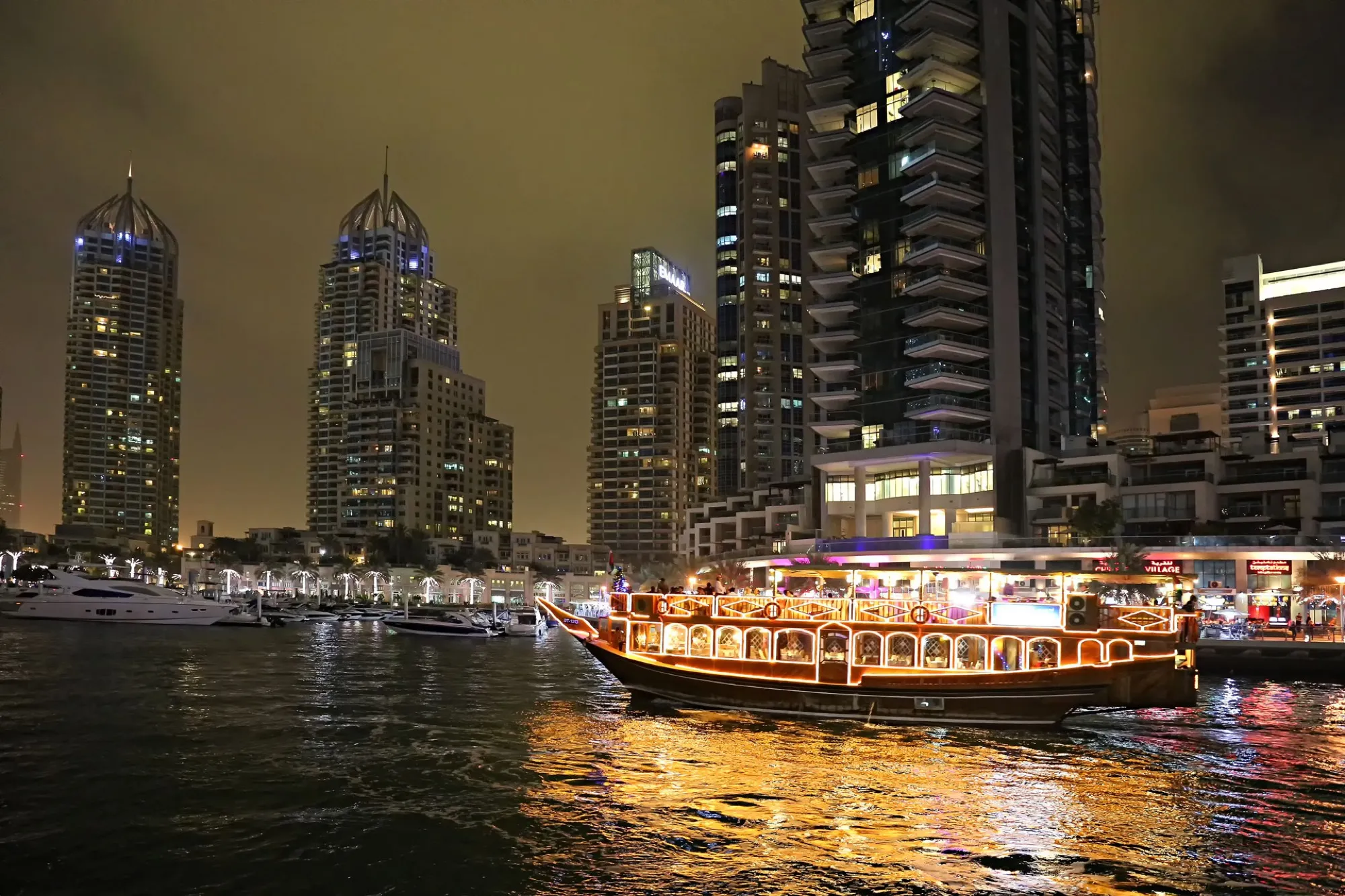 A lit dhow cruise boat on the water at Dubai Marina at night, with towers behind