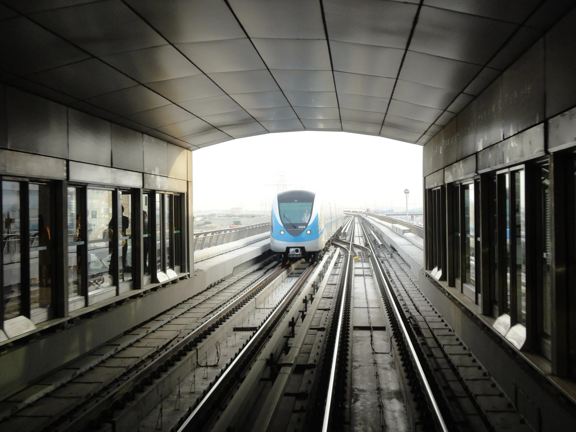 A blue Dubai Metro train approaching along the raised track