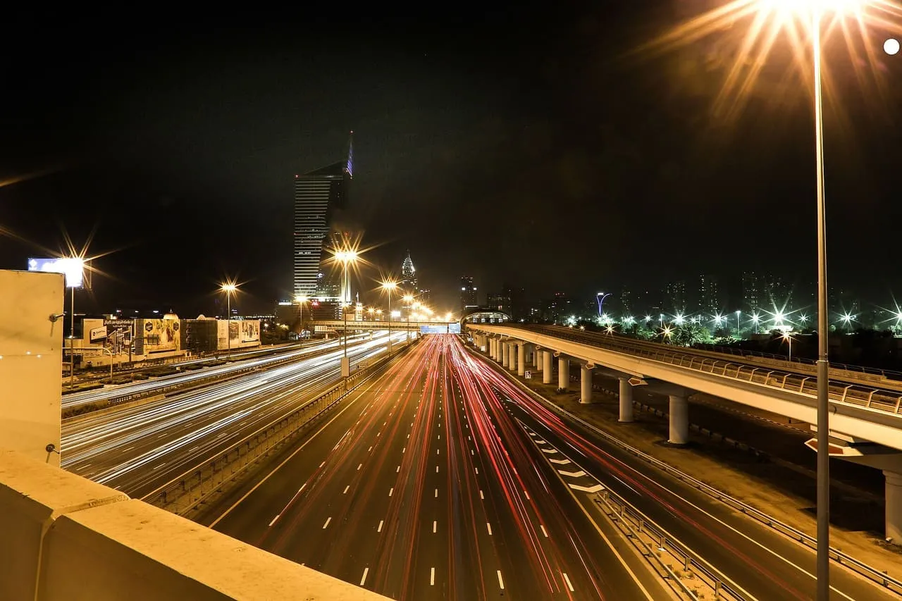 Night traffic light trails on a Dubai highway beside the Metro viaduct