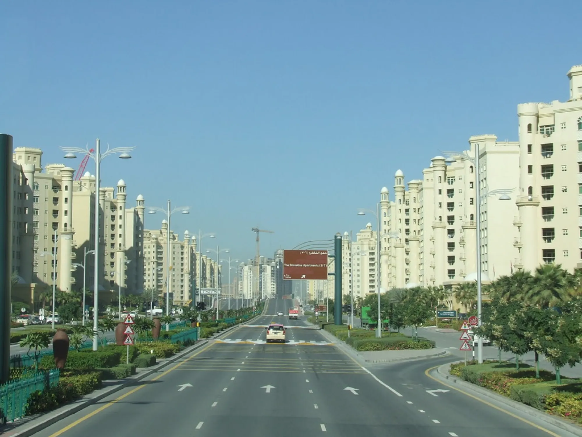 A wide road lined with beige apartment towers on Palm Jumeirah, seen from the top deck of a Dubai sightseeing bus