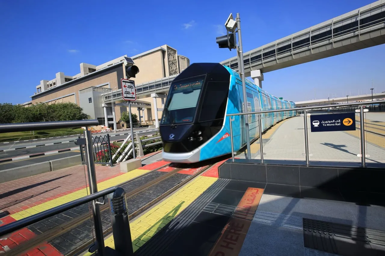 A Dubai Tram at a stop, with a sign pointing passengers to the Palm Monorail