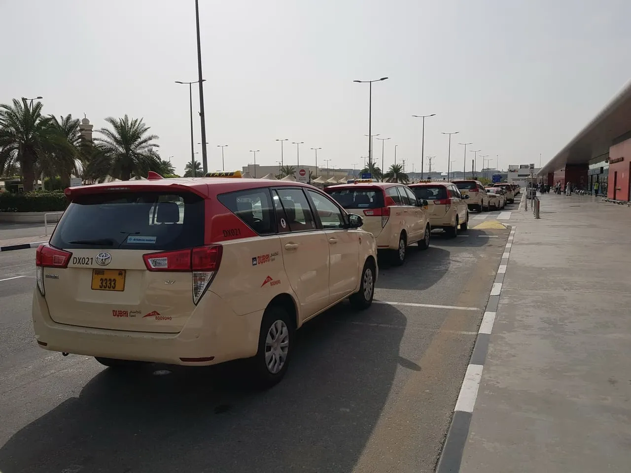 A line of red-roof Dubai Taxi cars waiting at the rank outside DXB Terminal 2