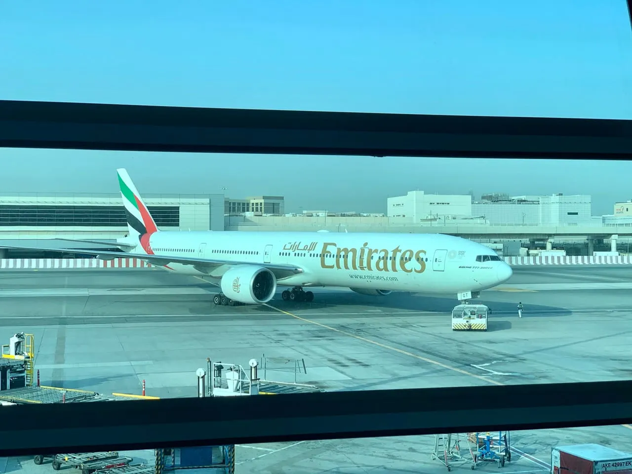 An Emirates Boeing 777 on the apron, seen through the window of Terminal 3 at Dubai International Airport