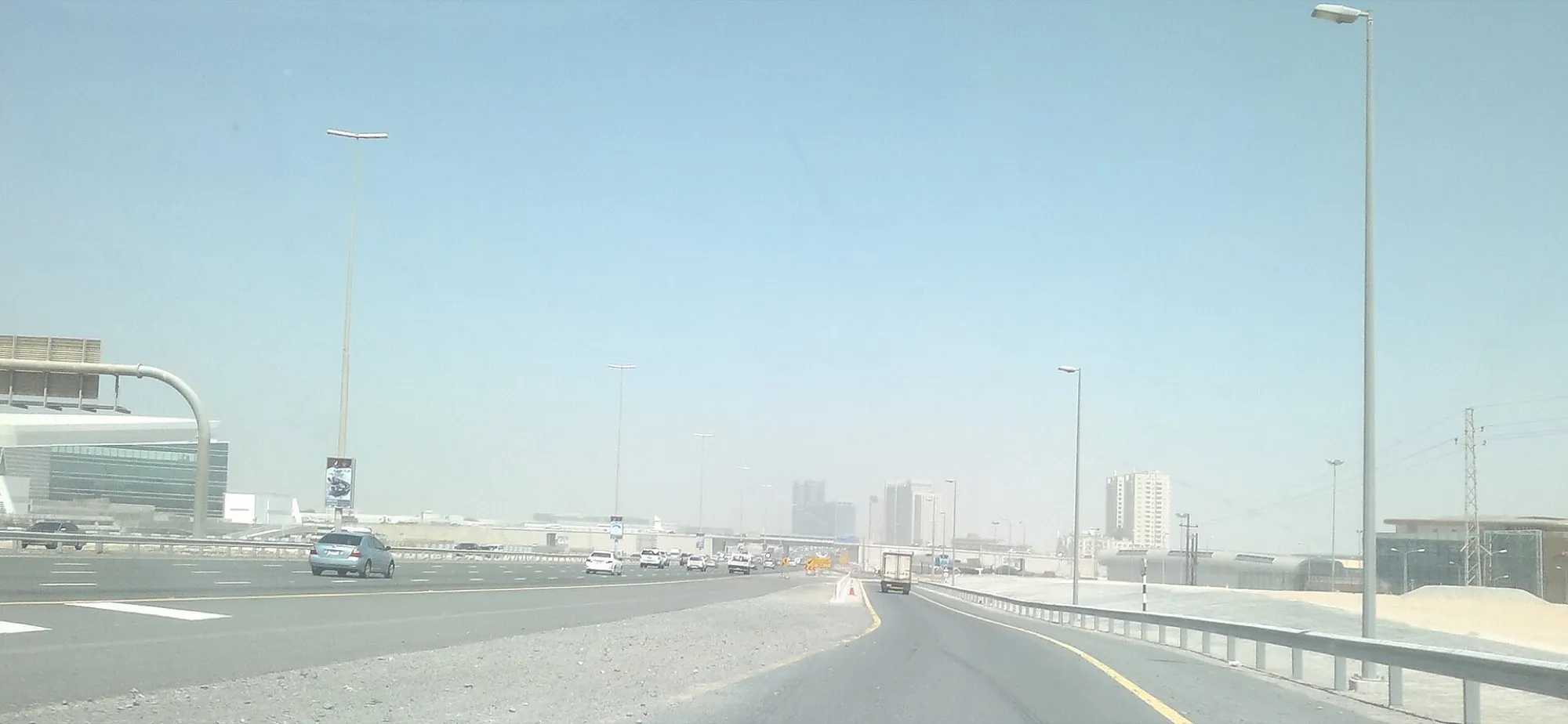 Multi-lane E11 highway out of Dubai on a hazy day, with a lorry and cars heading towards the Abu Dhabi side