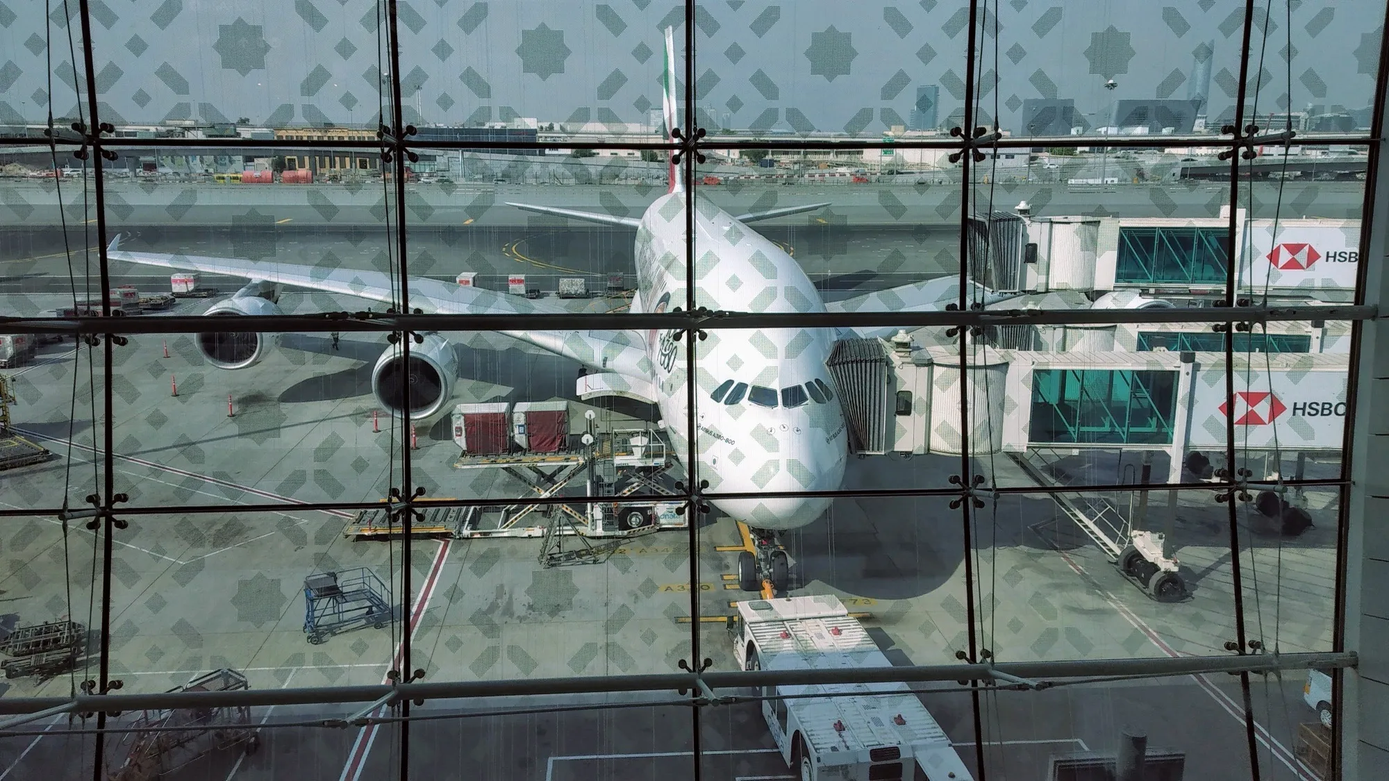 An Emirates Airbus A380 at a gate at Dubai International, seen through the patterned glass of the terminal