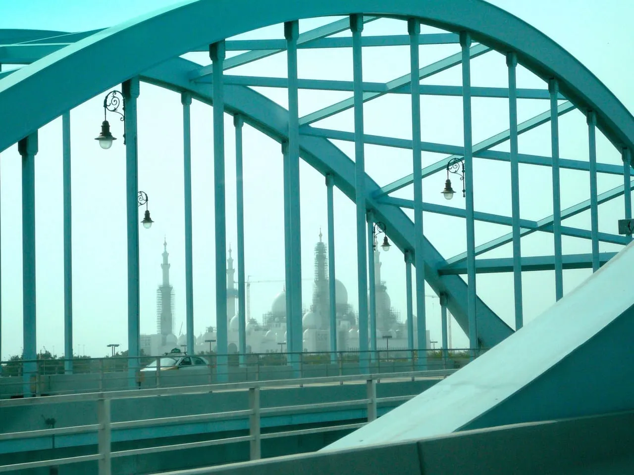 The domes and minarets of the Sheikh Zayed Grand Mosque seen through the green steel arches of Al Maqta Bridge