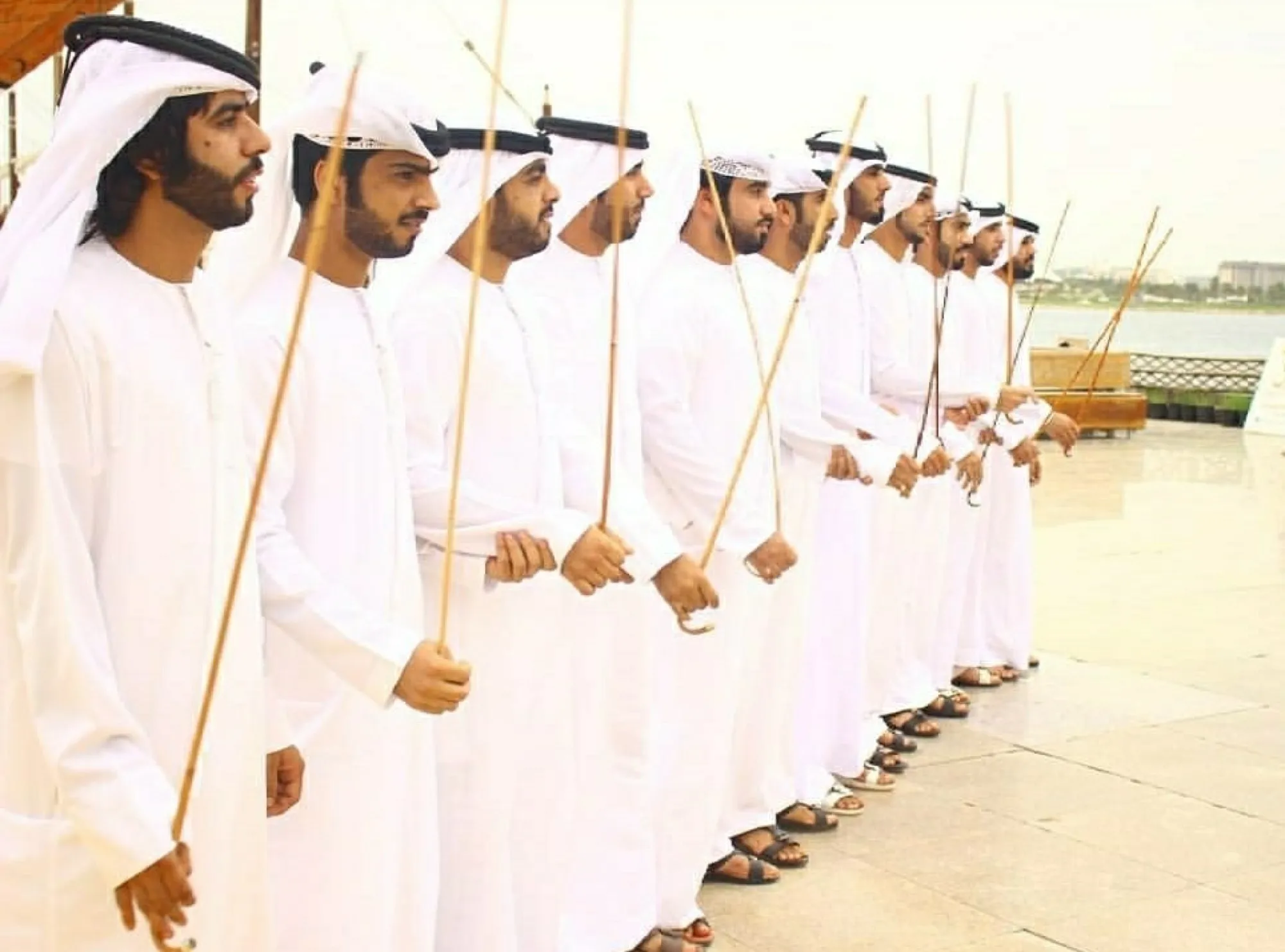 Men in white kandura performing a traditional Emirati group dance with canes