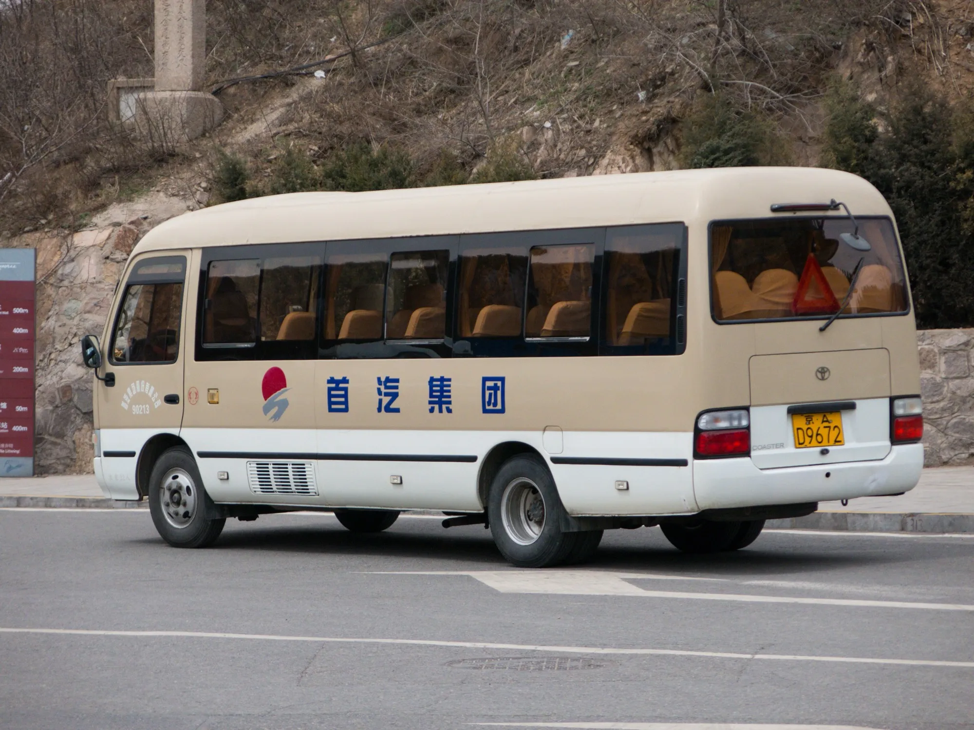 A Toyota Coaster midi bus parked beside a road, with its rear windows and luggage door visible