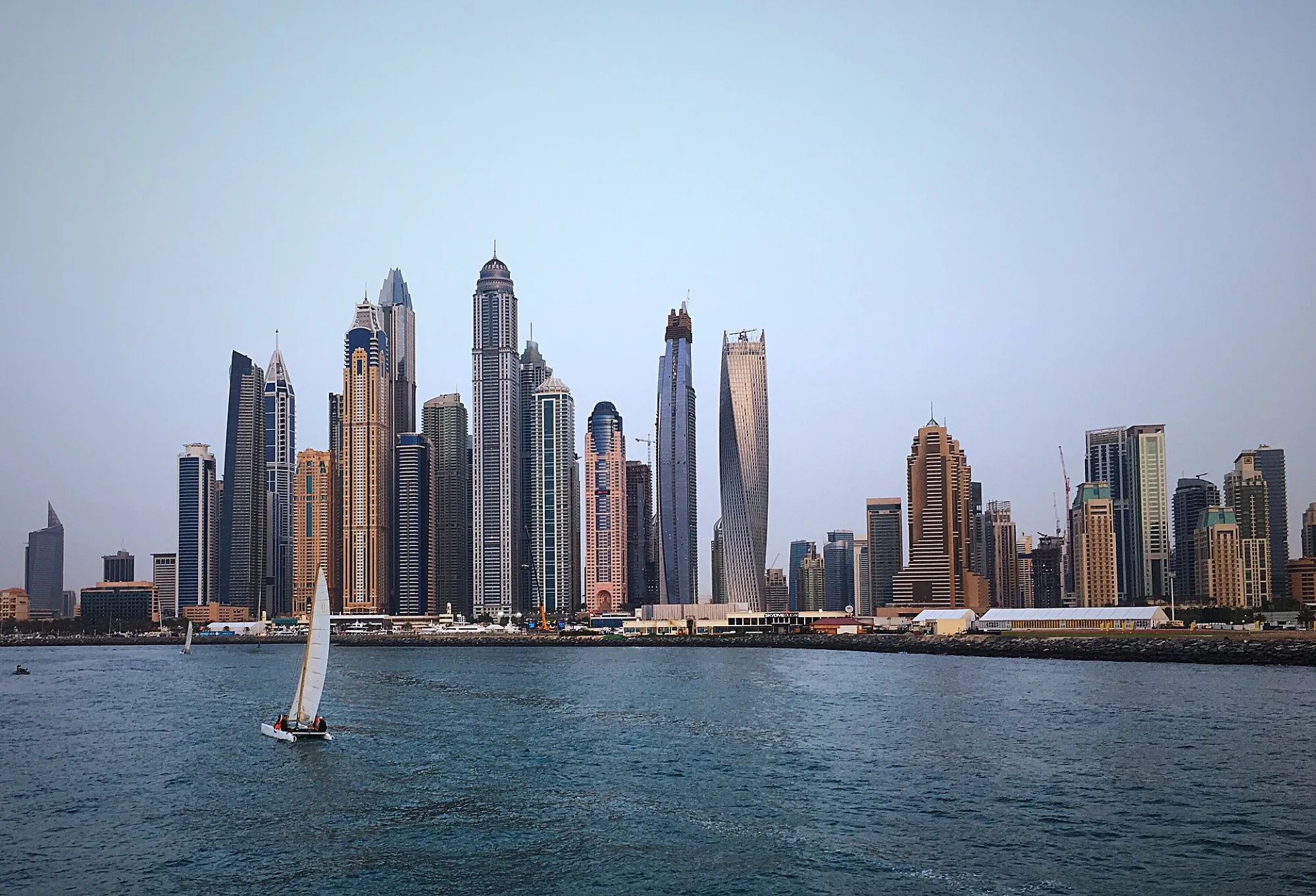 Dubai Marina towers seen from the water with a small sailing catamaran in the foreground