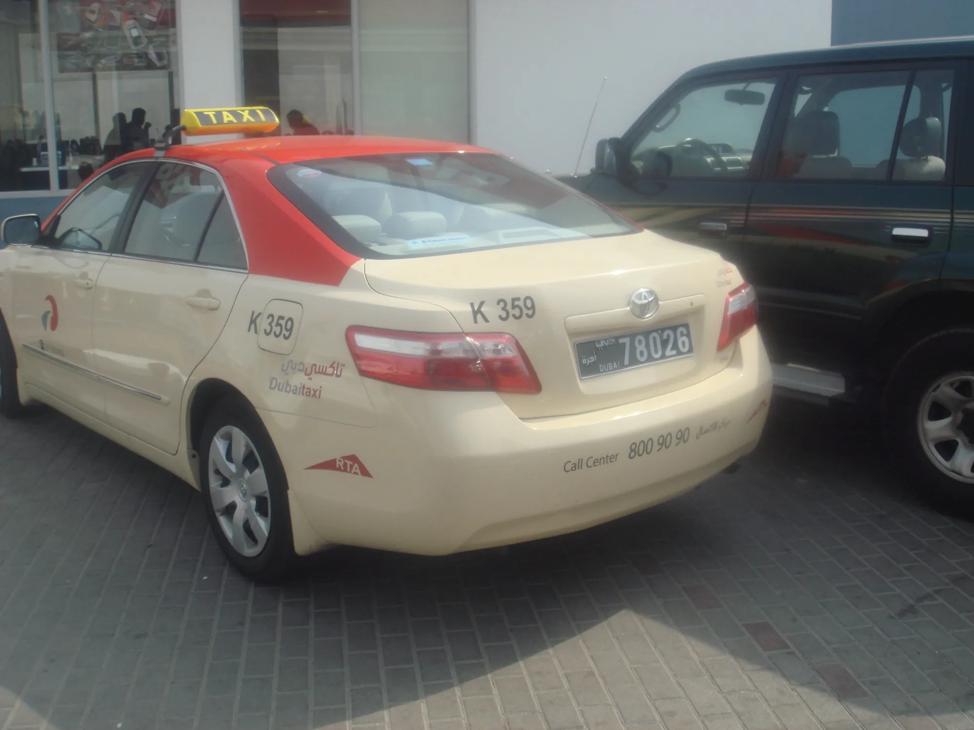 A cream Dubai Taxi with a red roof and a yellow TAXI roof sign, parked at the kerb