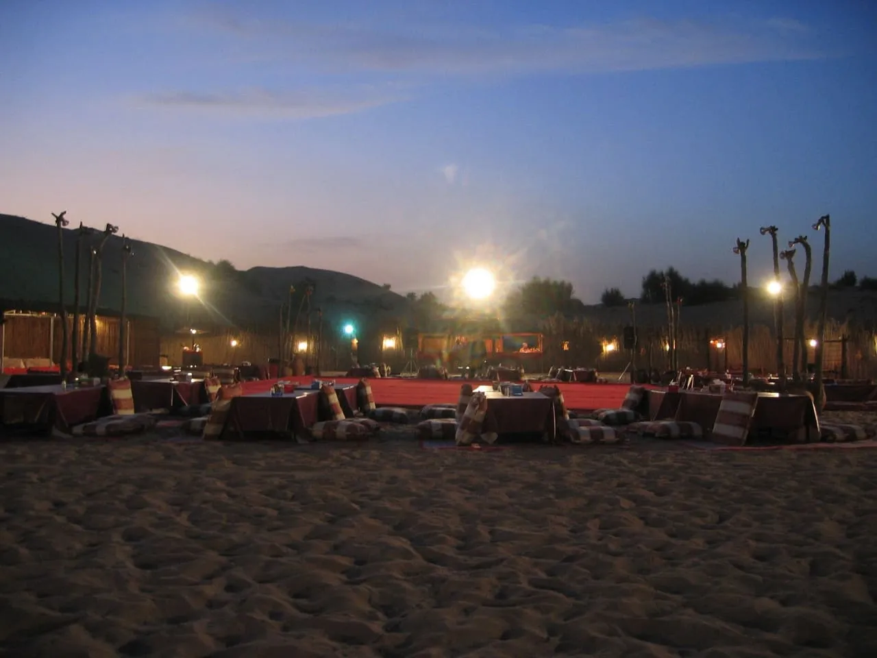 Low tables, floor cushions and lights set out on the sand at a desert camp outside Dubai at dusk