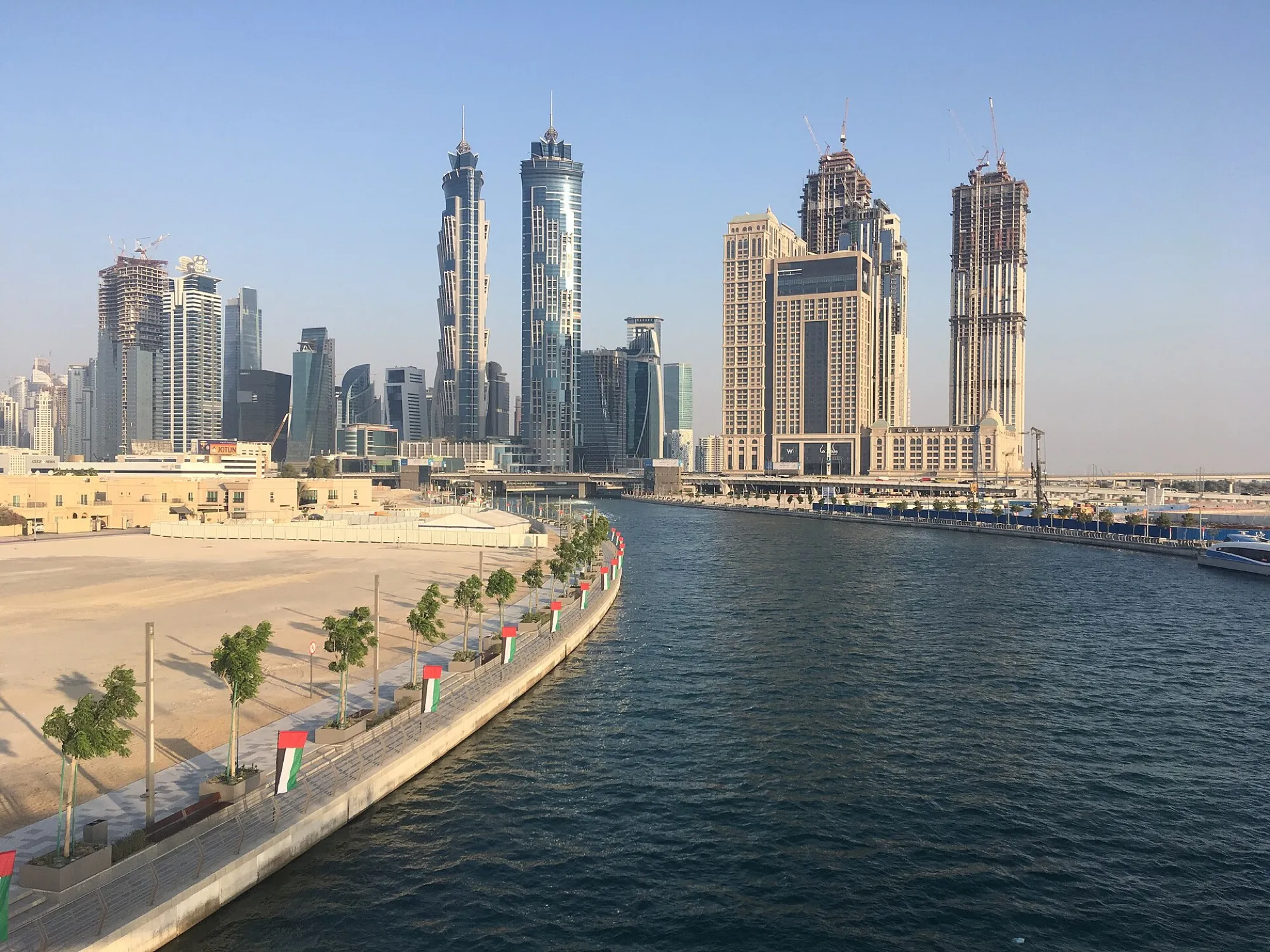 Business Bay towers beside the Dubai Water Canal, with UAE flags along the waterfront
