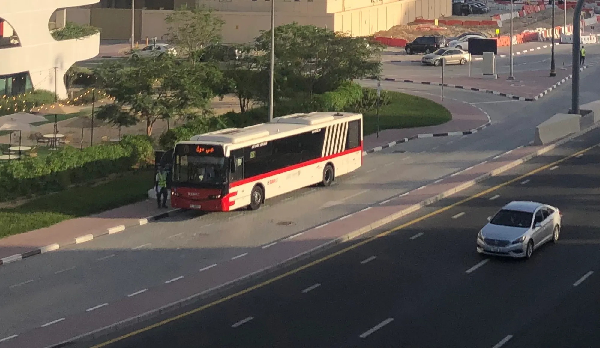 A red and white Dubai public bus stopped at a kerb beside a multi-lane road