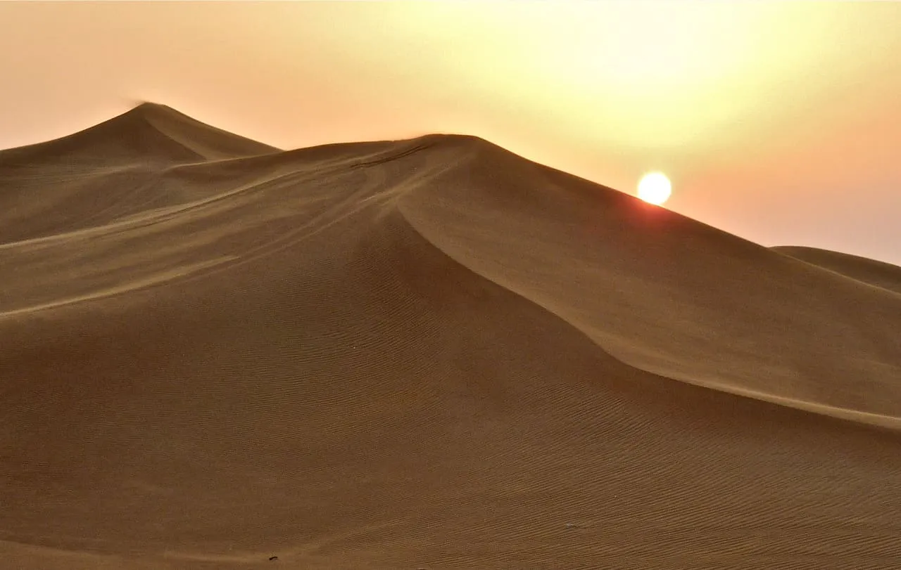 The sun setting behind a sand dune beside Al Awir Road in the Dubai desert
