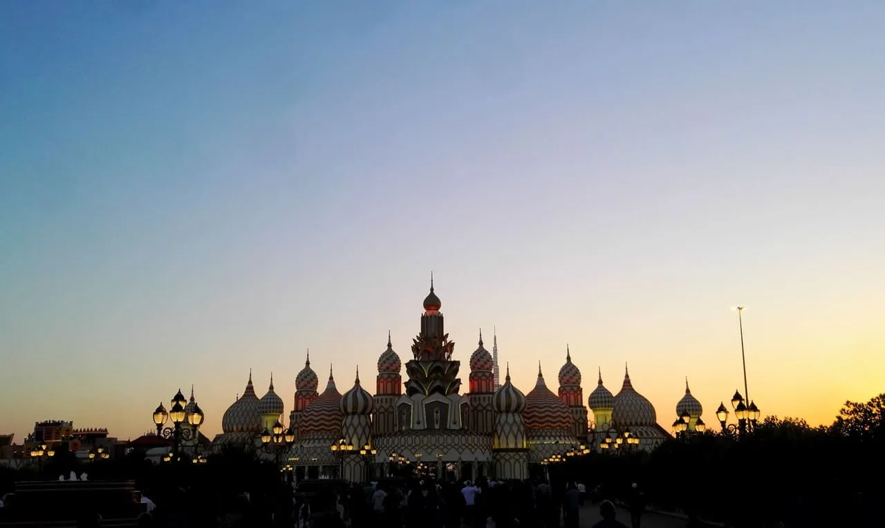The domed main gate of Global Village in Dubai at dusk, with its lamps lit