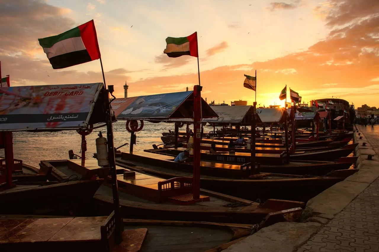 Wooden abras moored on Dubai Creek at sunset, with UAE flags on their canopies