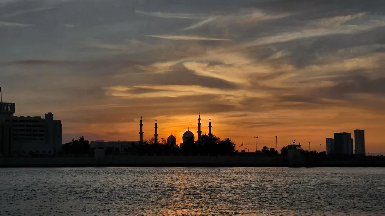 The domes and minarets of the Sheikh Zayed Grand Mosque in silhouette at sunset, across the water in Abu Dhabi