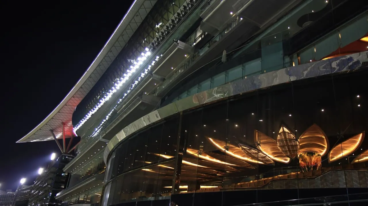 The Meydan Grandstand at night, its curved roof and glass-fronted levels lit up beside the racecourse in Nad Al Sheba, Dubai