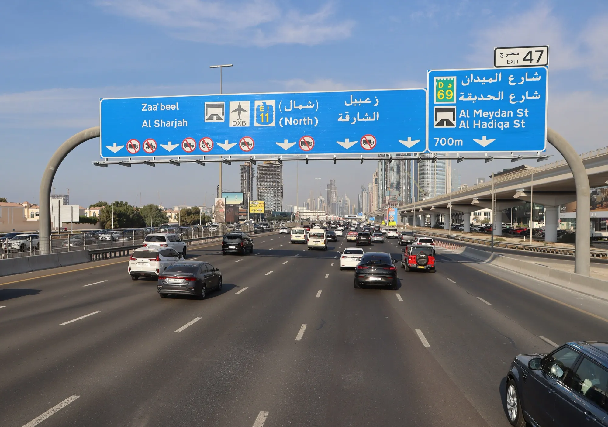 Traffic on Sheikh Zayed Road in Dubai under overhead signs for Sharjah, DXB airport and Al Meydan Street