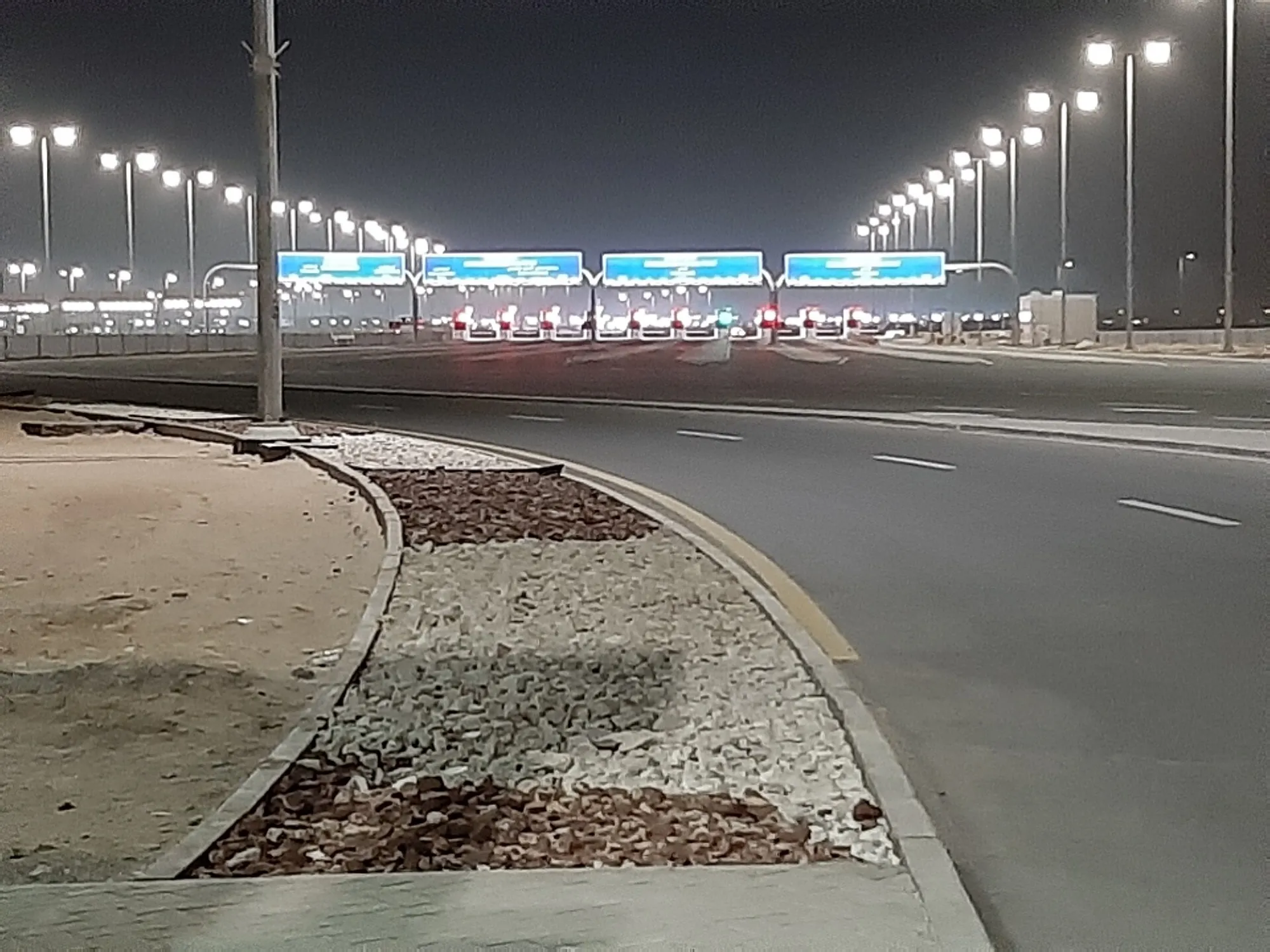 The Al Ghuwaifat border gates at night, with blue overhead signs above the lanes and a long lit approach road