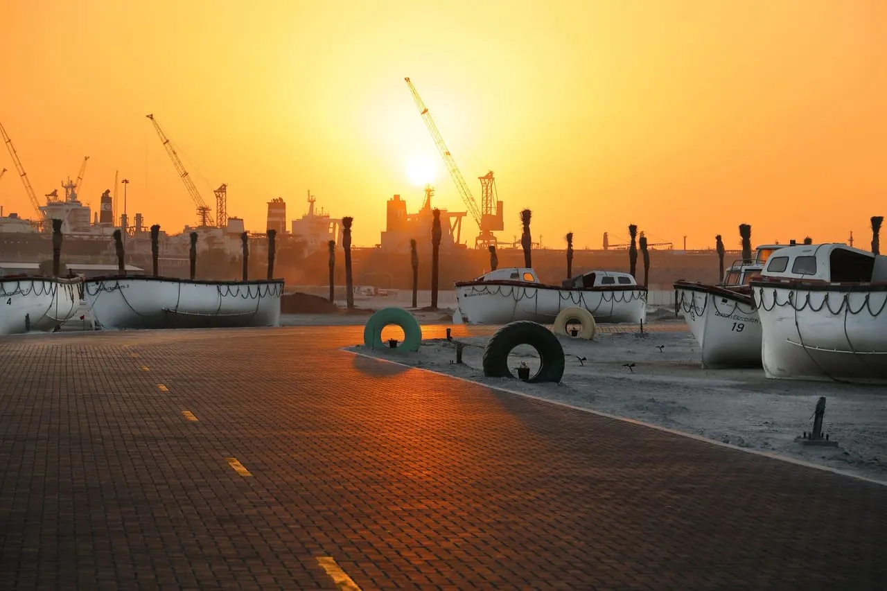 Sunset over the cranes and ships at Port Rashid, Dubai, with white lifeboats on the quay