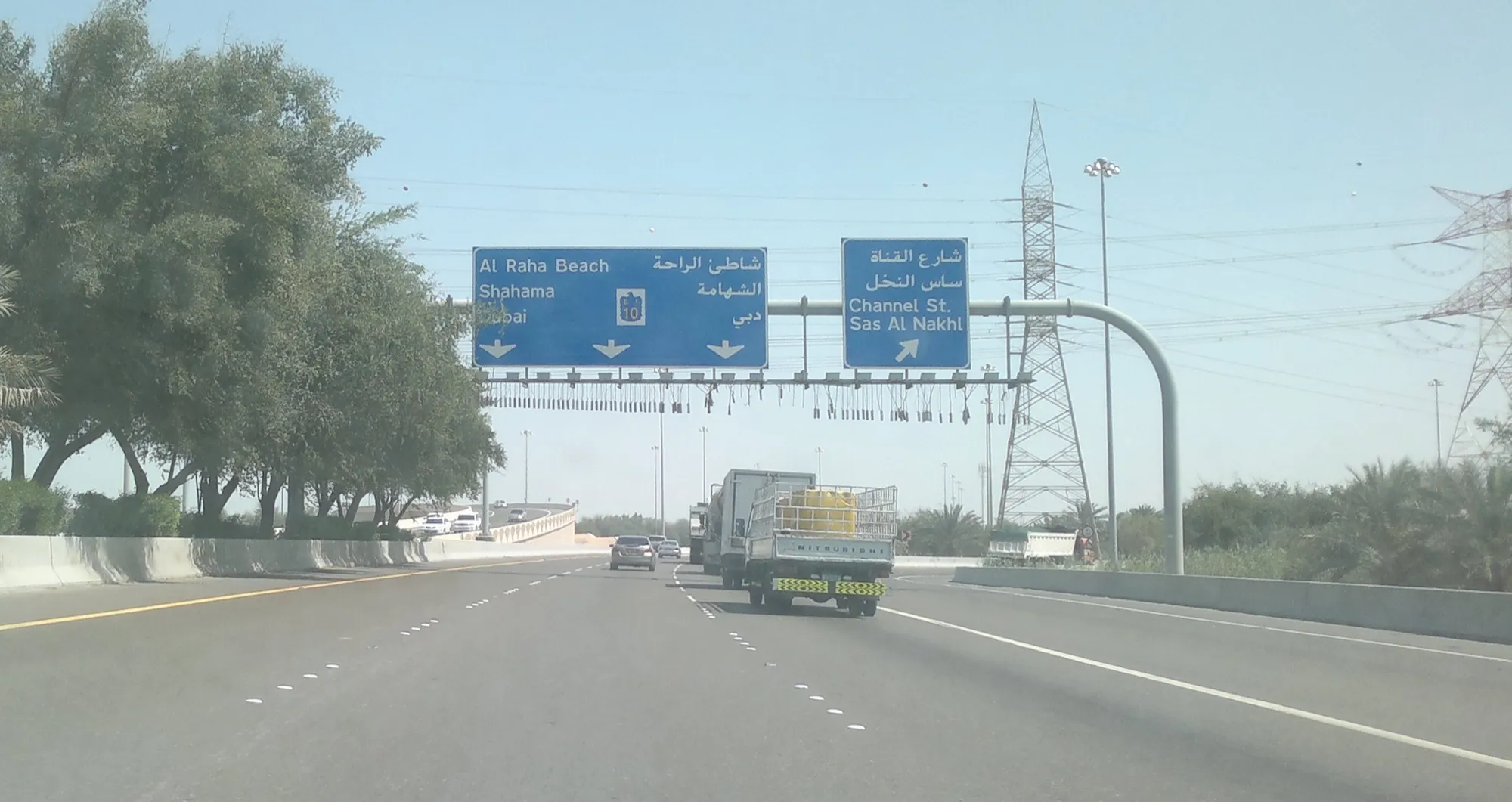 Overhead signs on a road in Abu Dhabi pointing ahead to Al Raha Beach, Shahama and Dubai