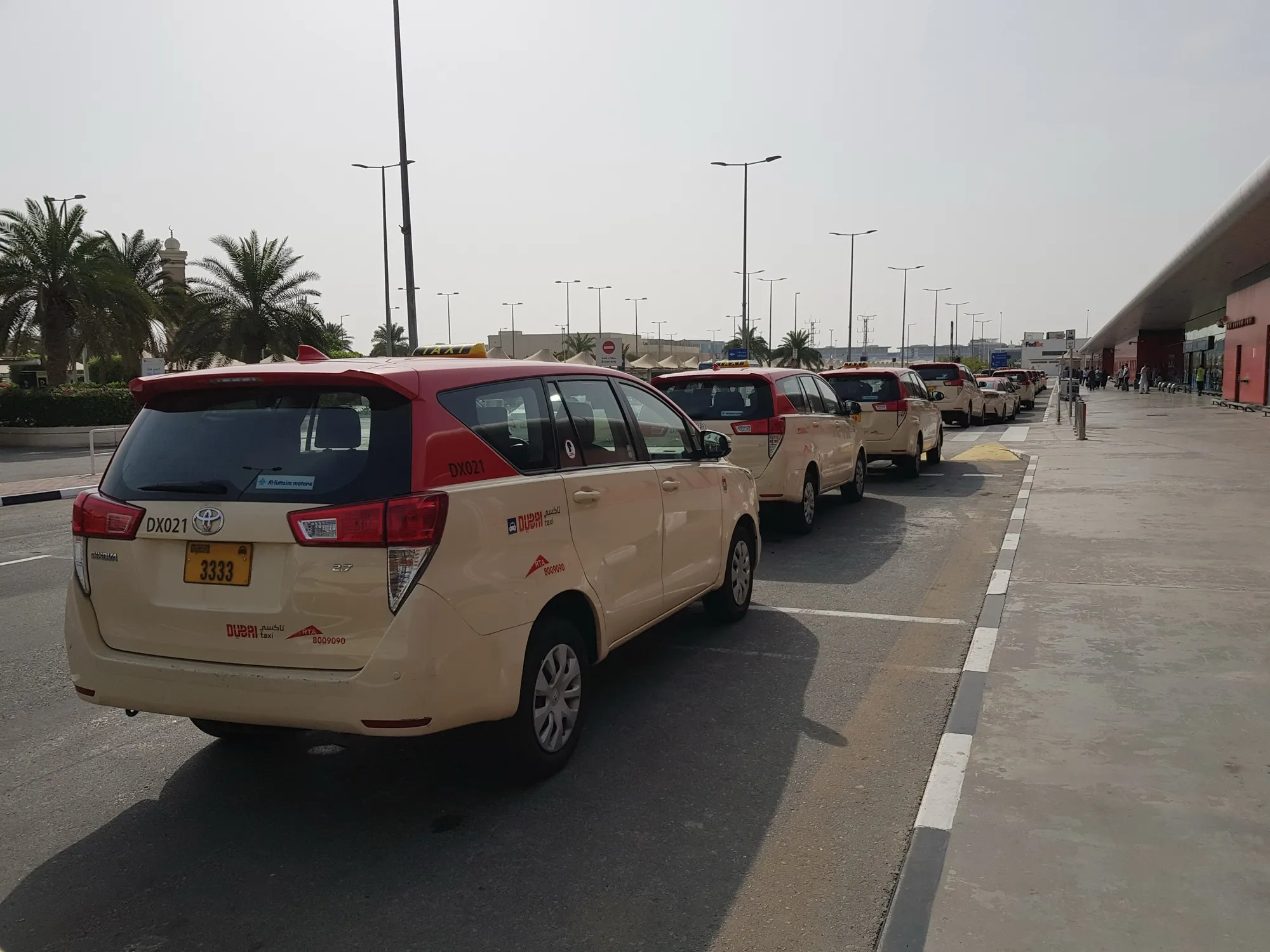 A line of cream Dubai Taxi cars waiting at a taxi rank outside Dubai International Airport