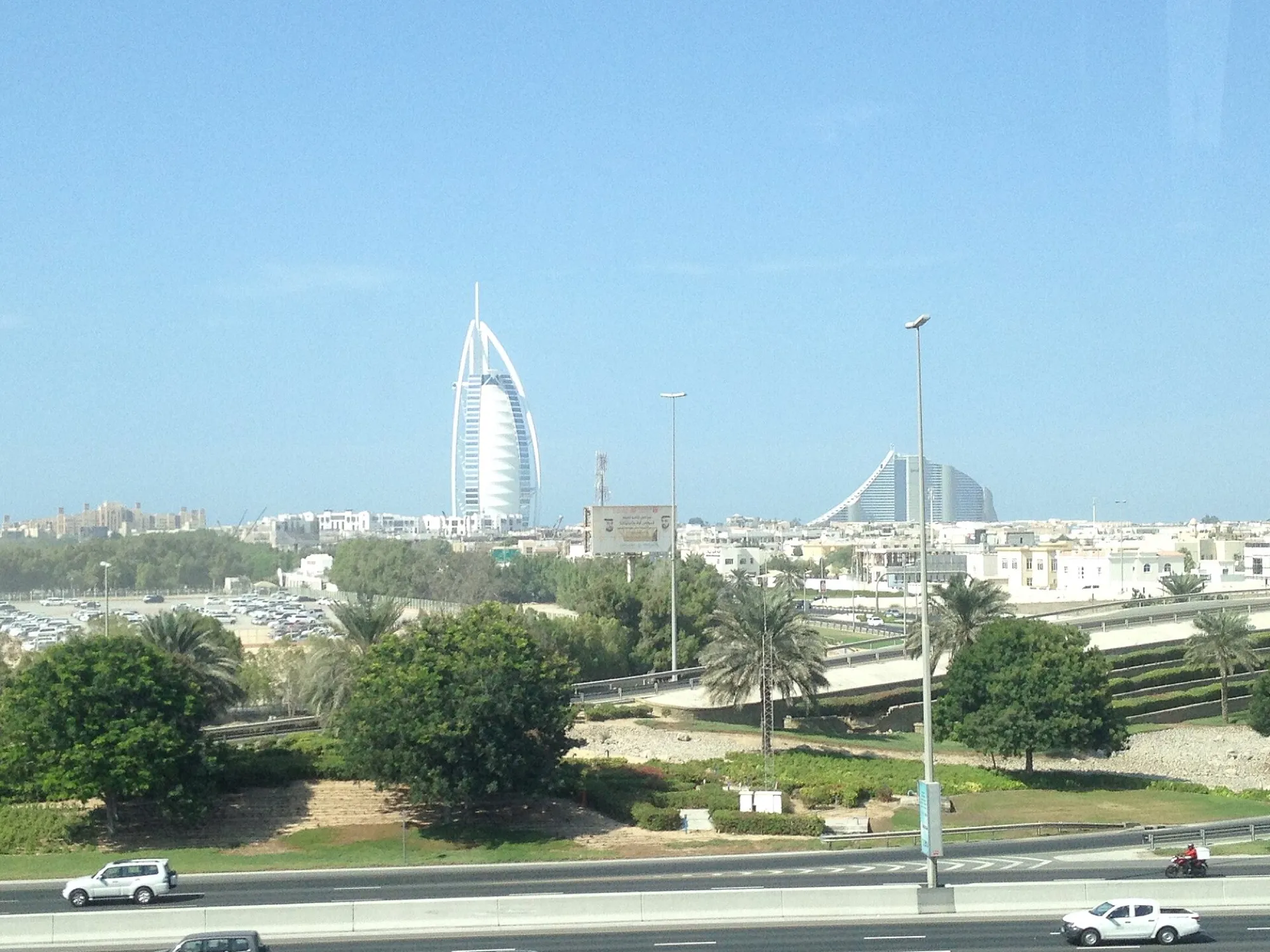 The Burj Al Arab hotel on the Dubai coast, seen across a road and palm trees