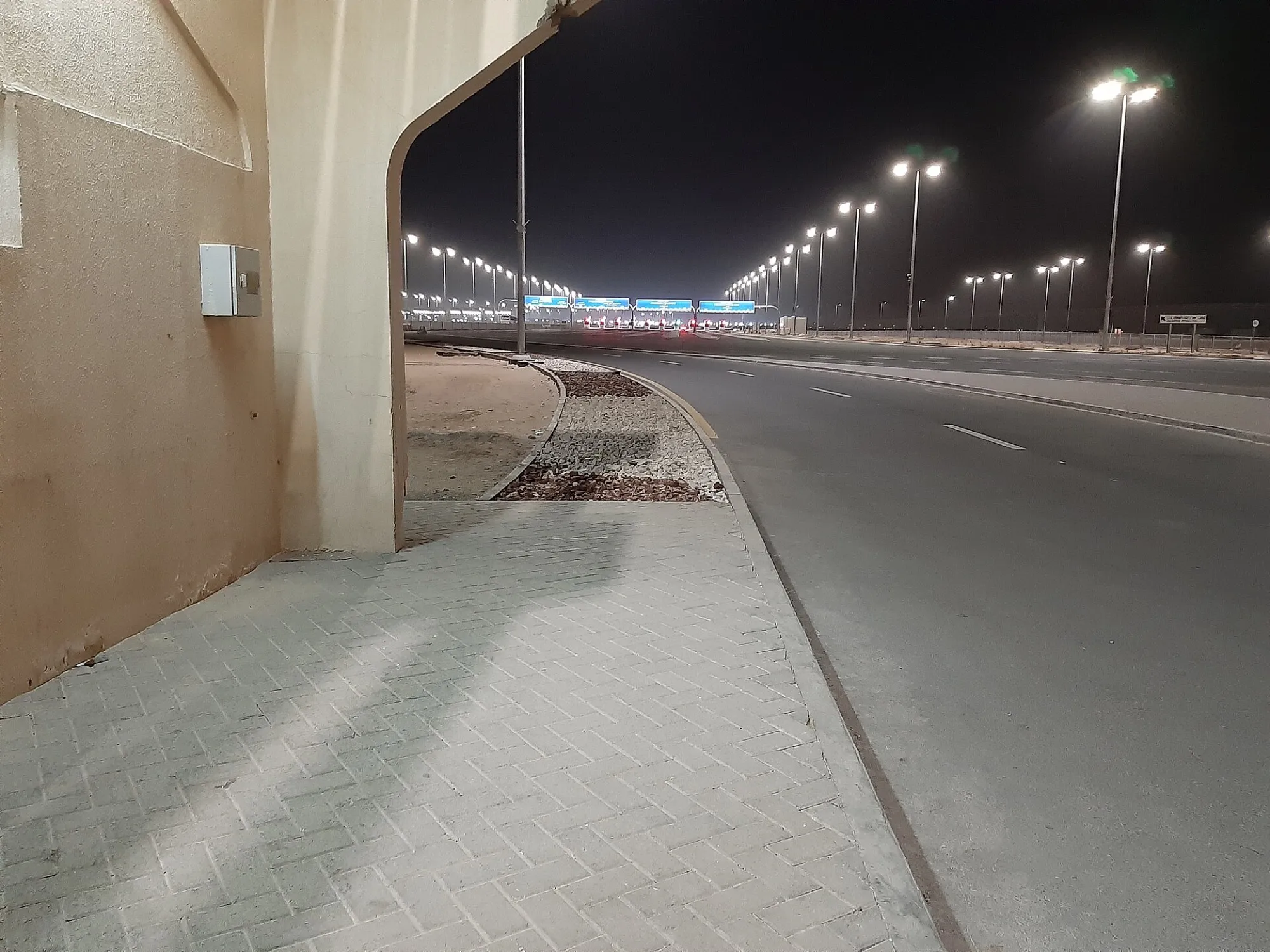 The Al Ghuwaifat border post seen from beside a building arch, with the lit road and signs ahead