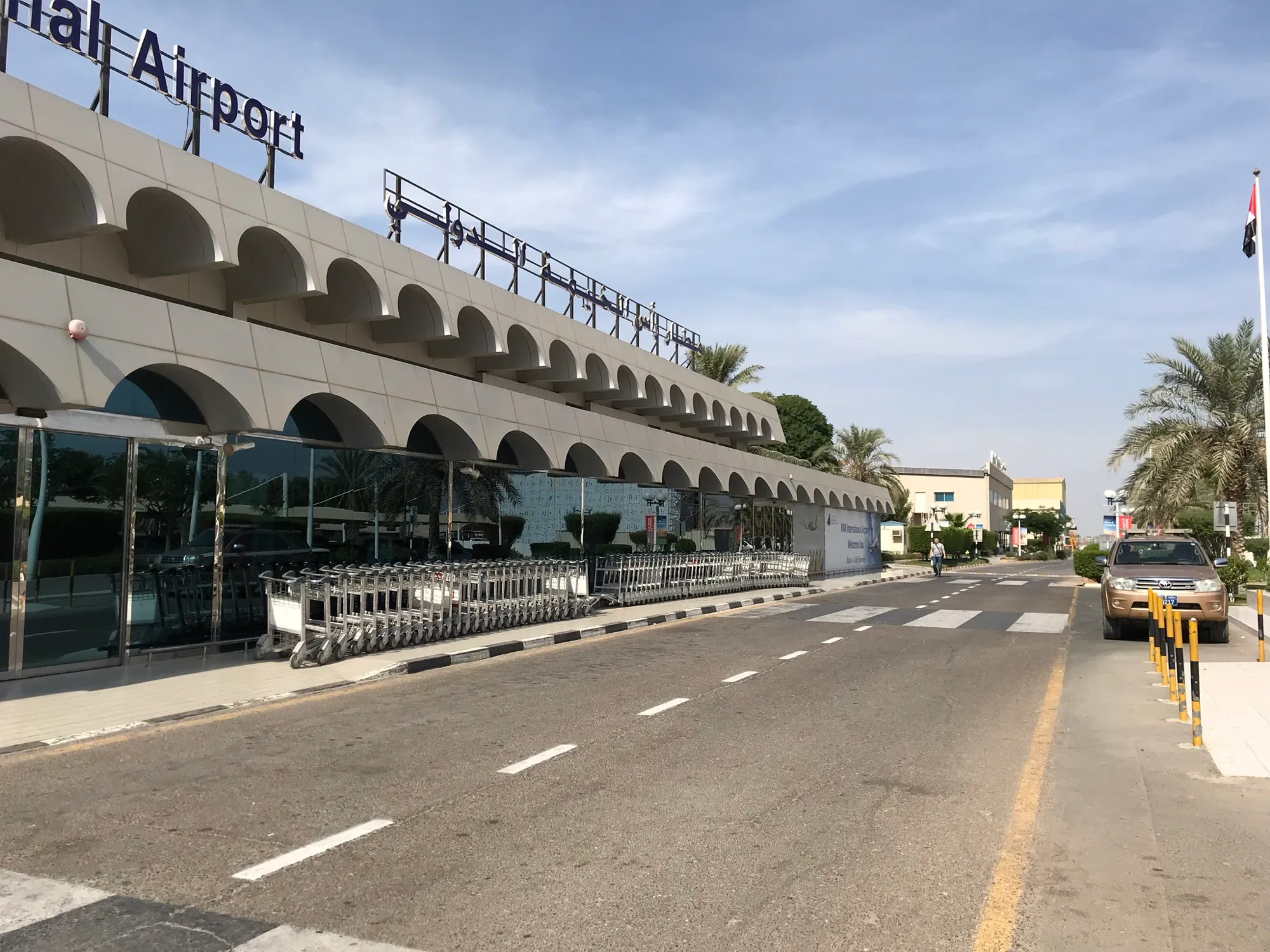 The arched front of the passenger terminal at Ras Al Khaimah International Airport, with palm trees and the forecourt road