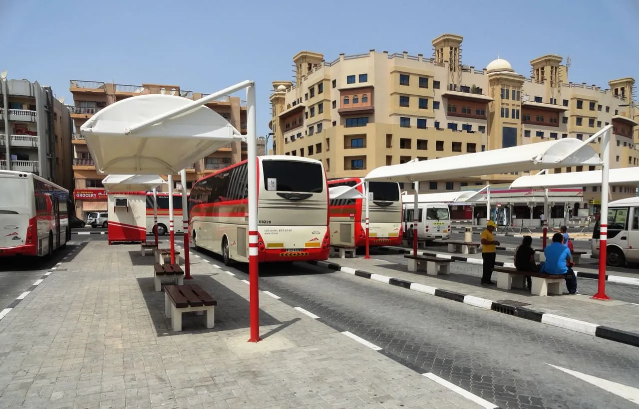 Red and white intercity coaches parked under shade canopies at the Bur Dubai bus station