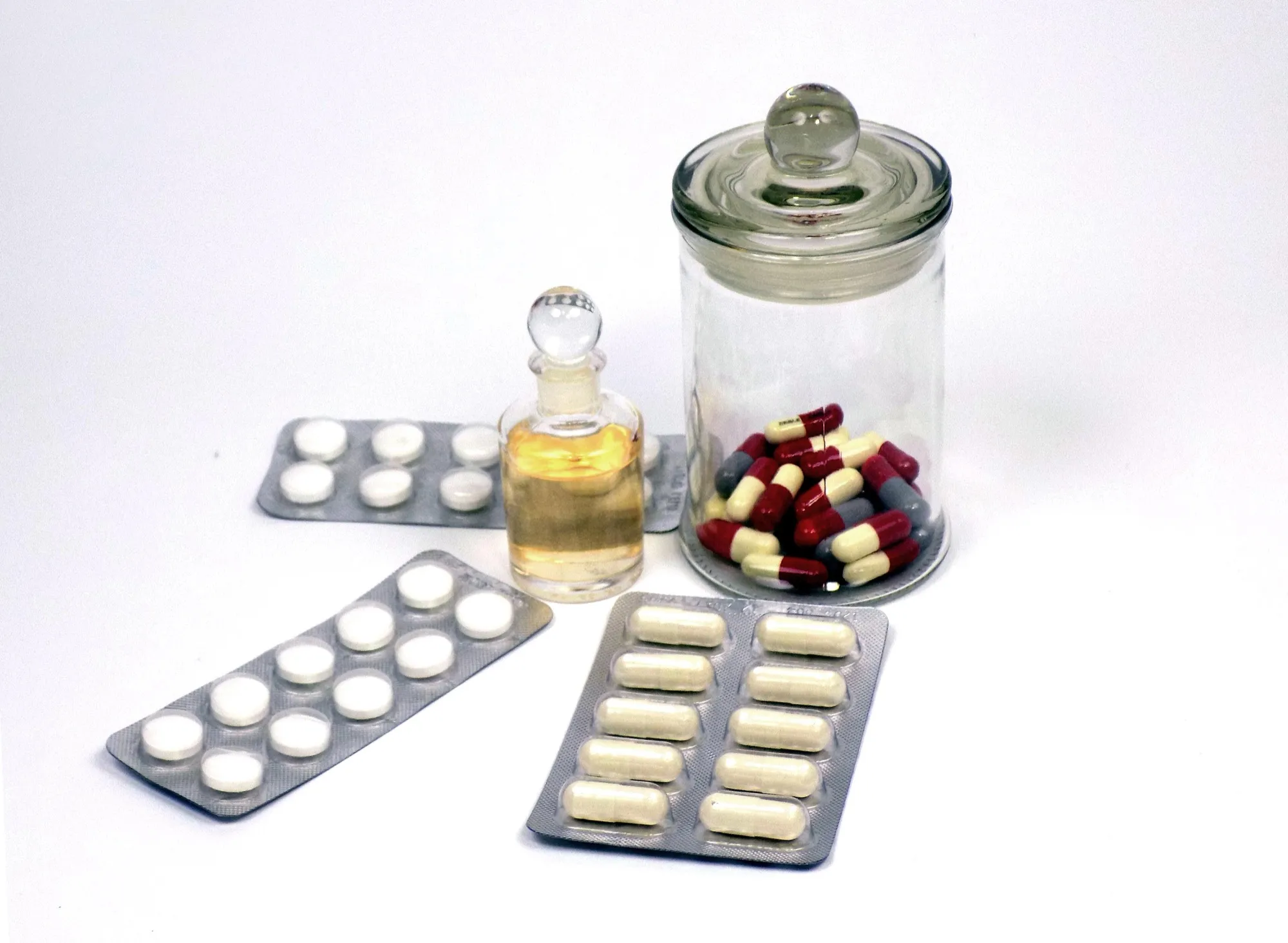 Blister packs of tablets and a glass jar of capsules on a white background