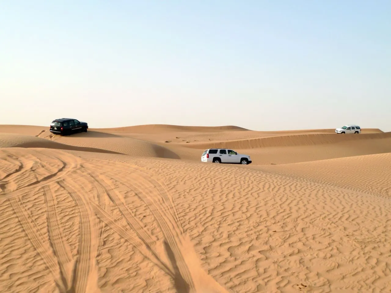 Three safari SUVs spread across the dunes outside Dubai, with tyre tracks in the sand