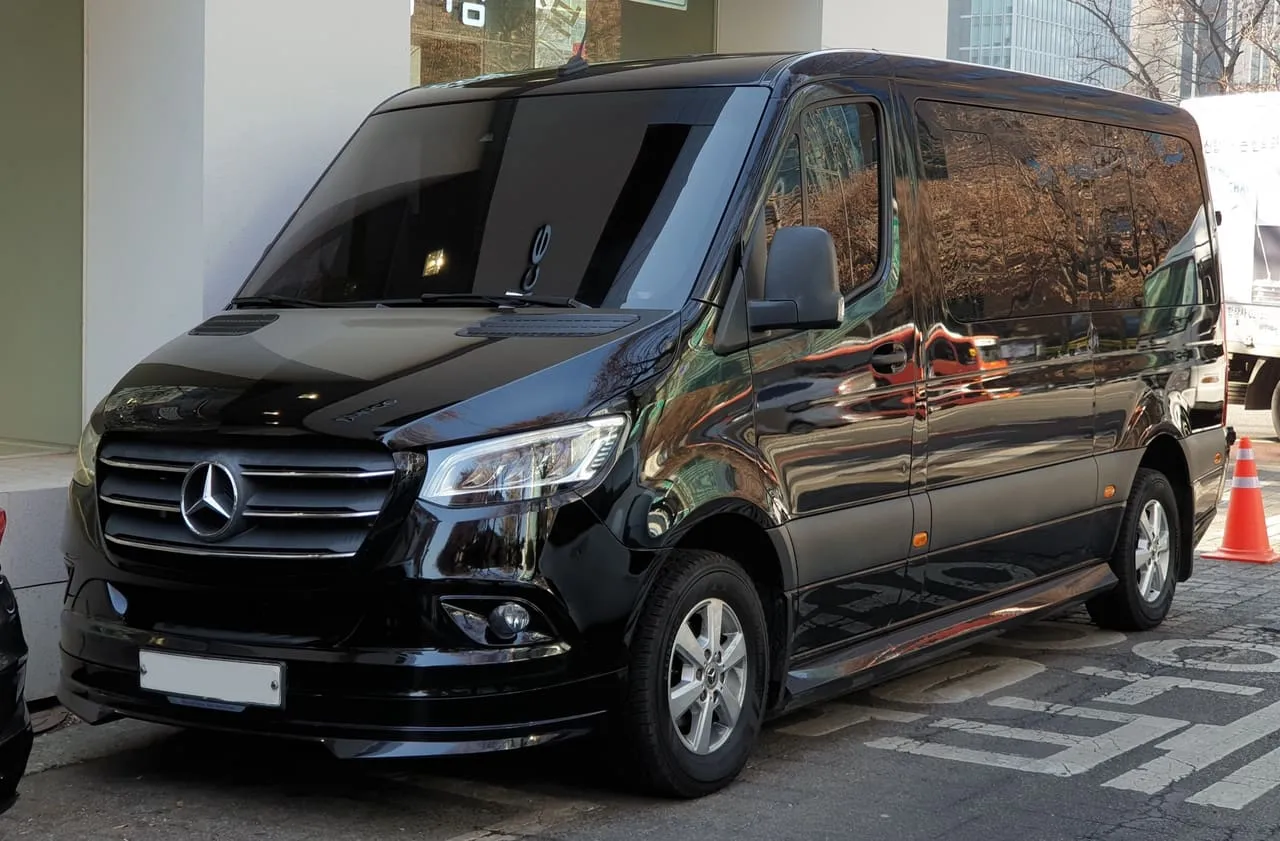 A black Mercedes-Benz Sprinter Tourer passenger van with tinted side windows, parked at the kerb