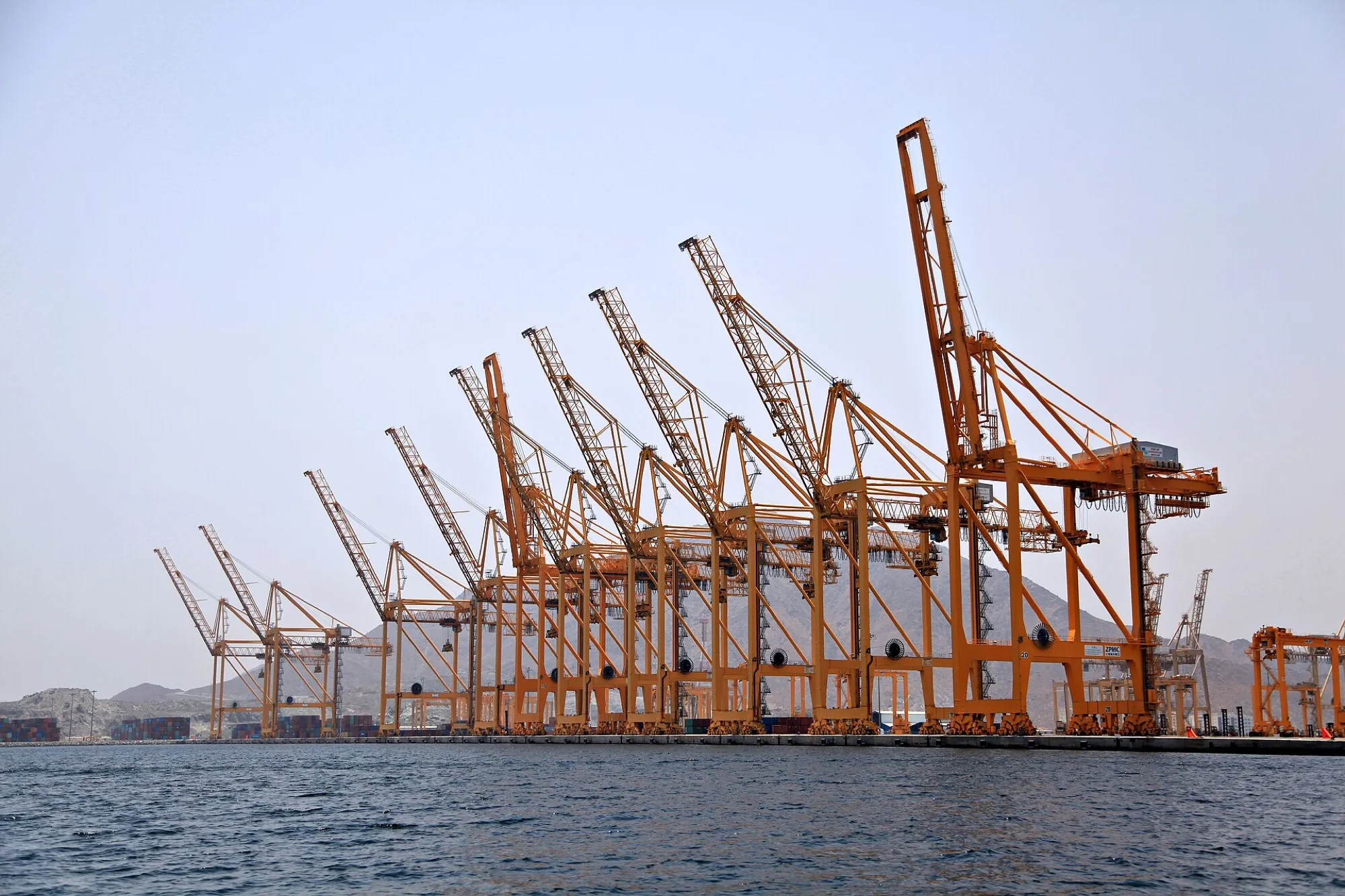 Quayside container cranes at Khor Fakkan port on the Gulf of Oman, with the Hajar Mountains behind